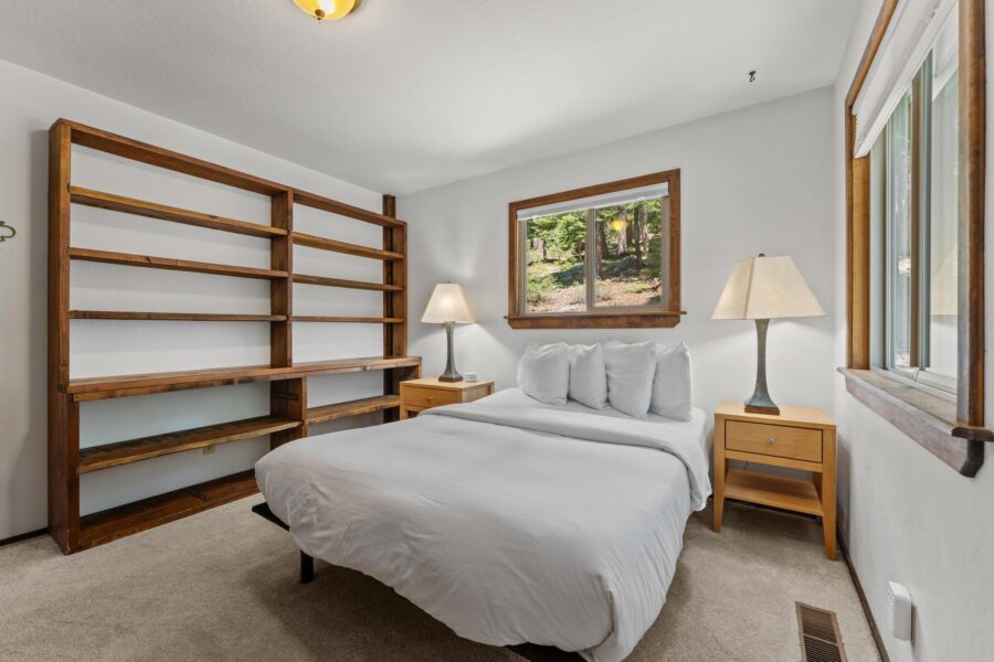 Bedroom in Tahoe Vista vacation rental with a cozy bed, wooden shelves, nightstands, lamps, and a forest view window.