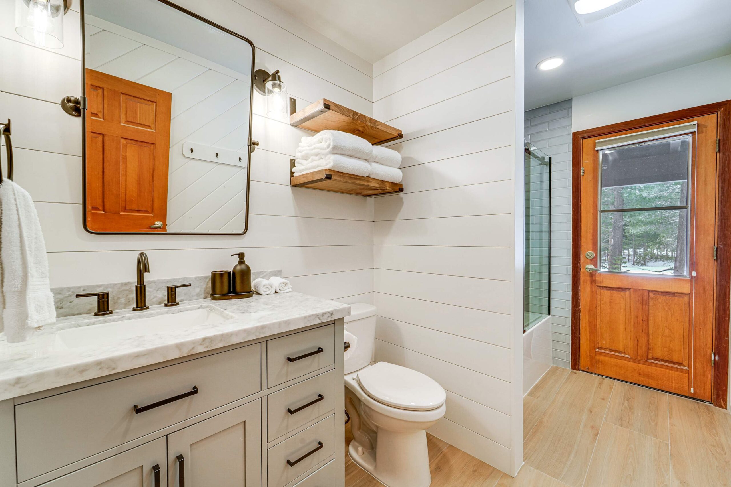 Modern bathroom in a Truckee vacation rental with white shiplap walls, wood accents, and a view of the outdoors.