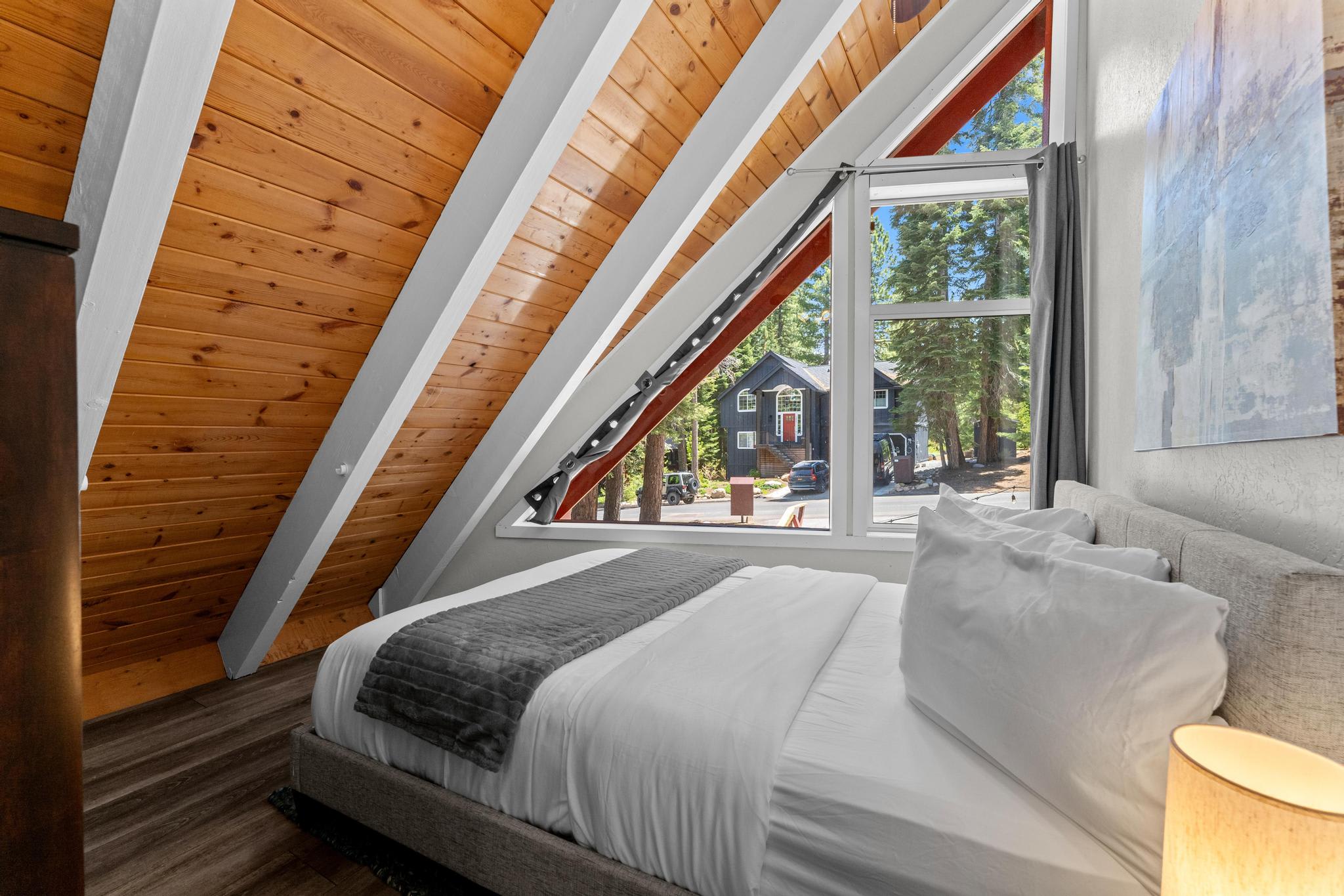 A cozy bedroom in a Tahoe Vista vacation rental with a rustic wooden ceiling and a large window with a scenic view.