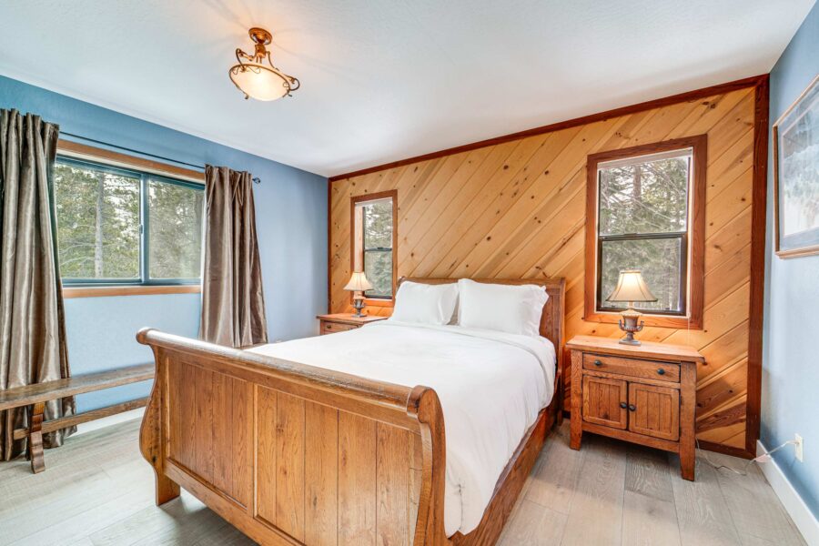 Cozy bedroom in a Truckee vacation rental with wooden bed, nightstands, and large windows overlooking nature.