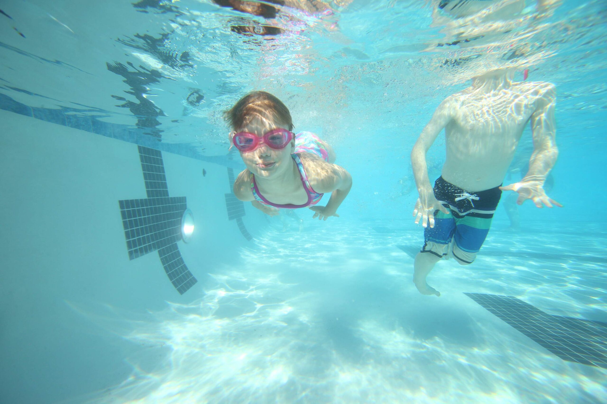 Children swim underwater in a clear pool at a Truckee vacation rental, enjoying a sunny day.