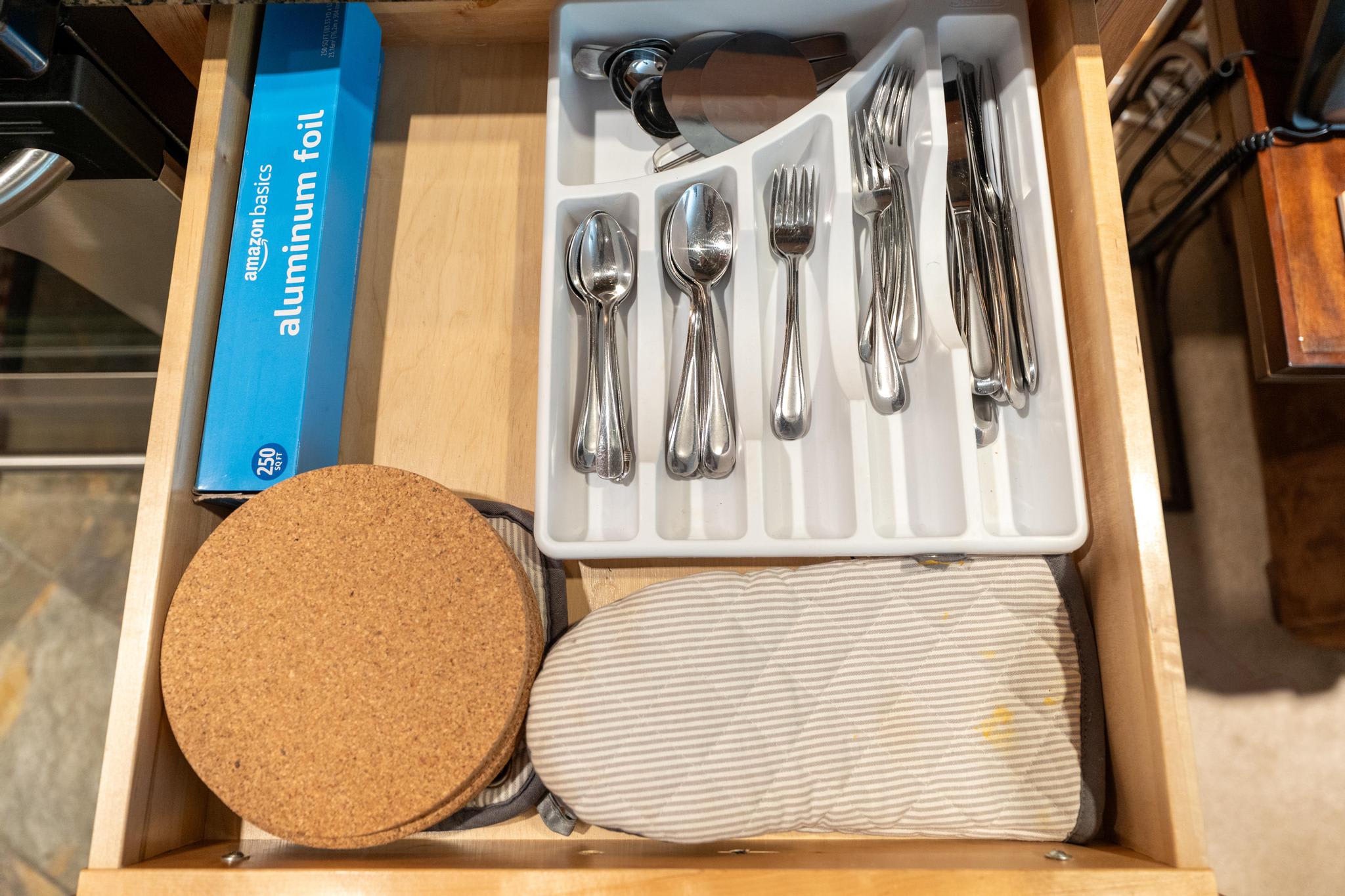 Open kitchen drawer in Truckee vacation rental with silverware, oven mitt, cork trivets, and aluminum foil.