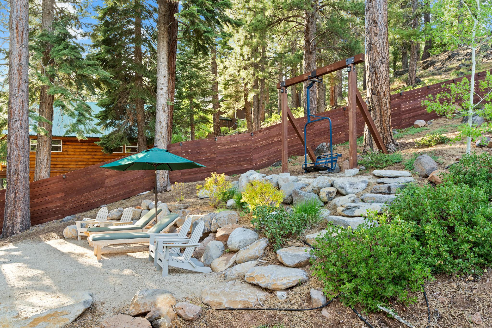 Outdoor area of a Truckee vacation rental with Adirondack chairs, loungers, umbrella, and forested view.