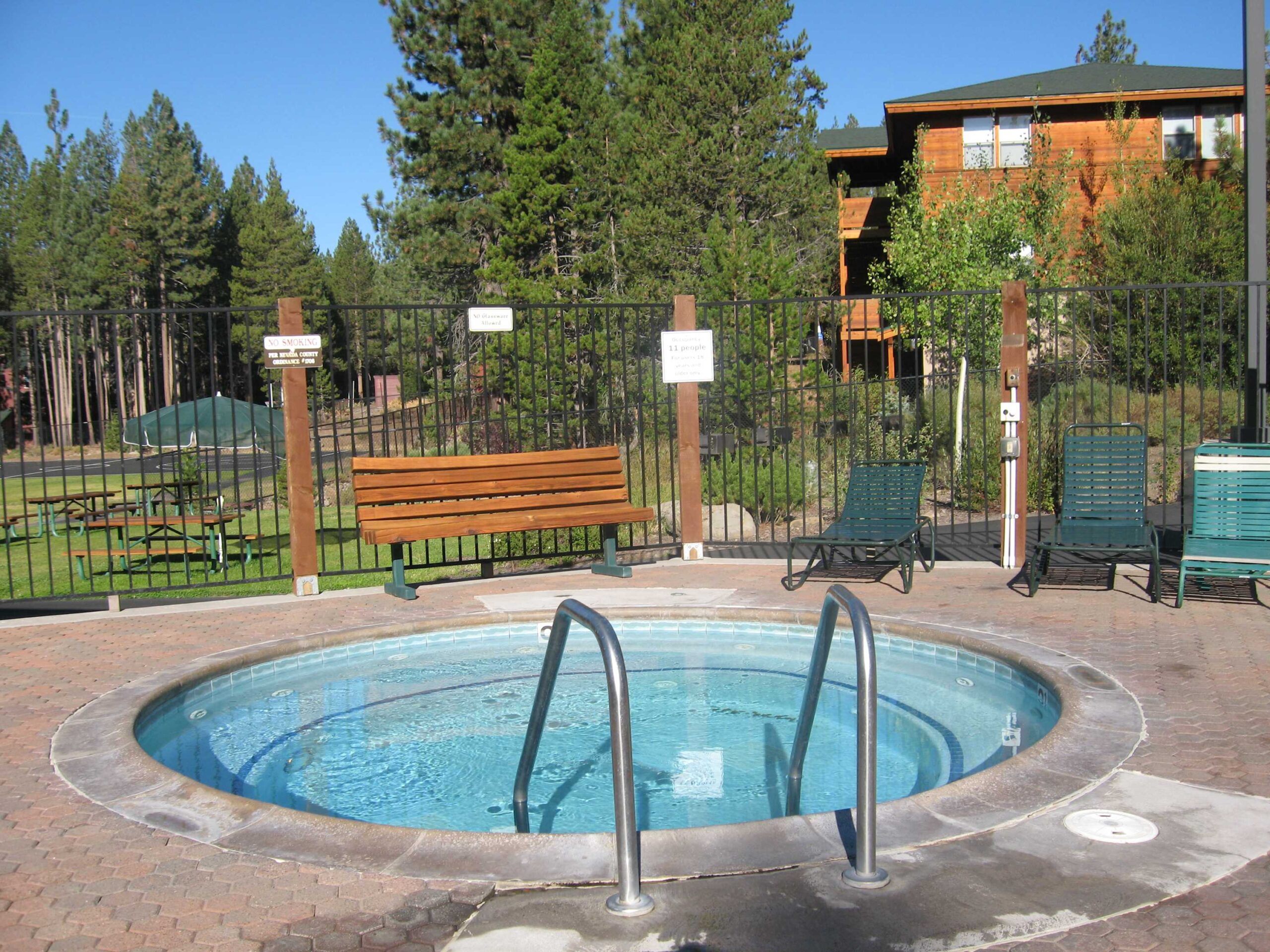 Outdoor hot tub at a Truckee vacation rental with surrounding trees, sunbathing chairs, and a rustic cabin in view.