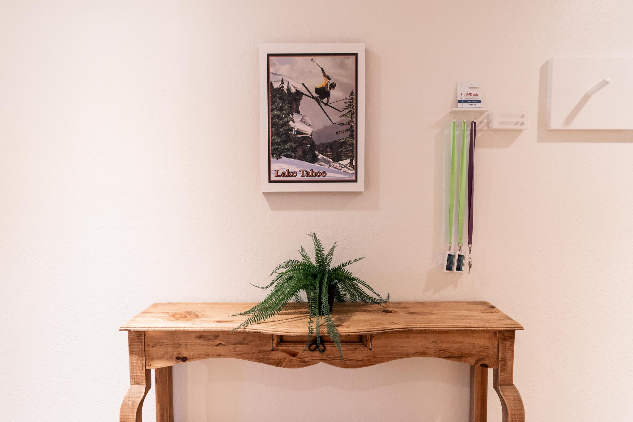 Wooden table with a fern, Lake Tahoe poster, and lanyards on a wall in a Truckee vacation rental.