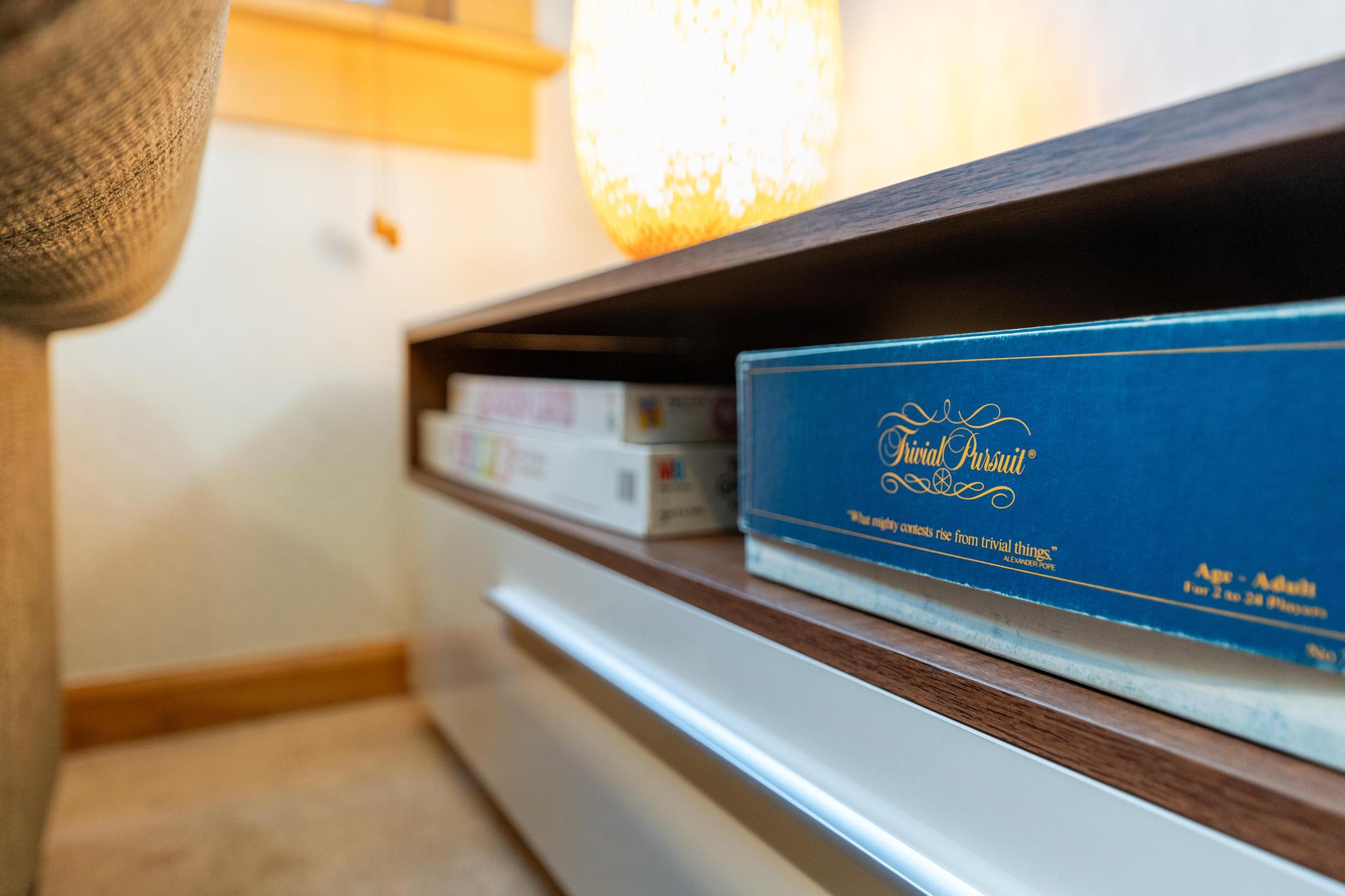Board games on a shelf in a Truckee vacation rental, including Trivial Pursuit under warm ambient lighting.
