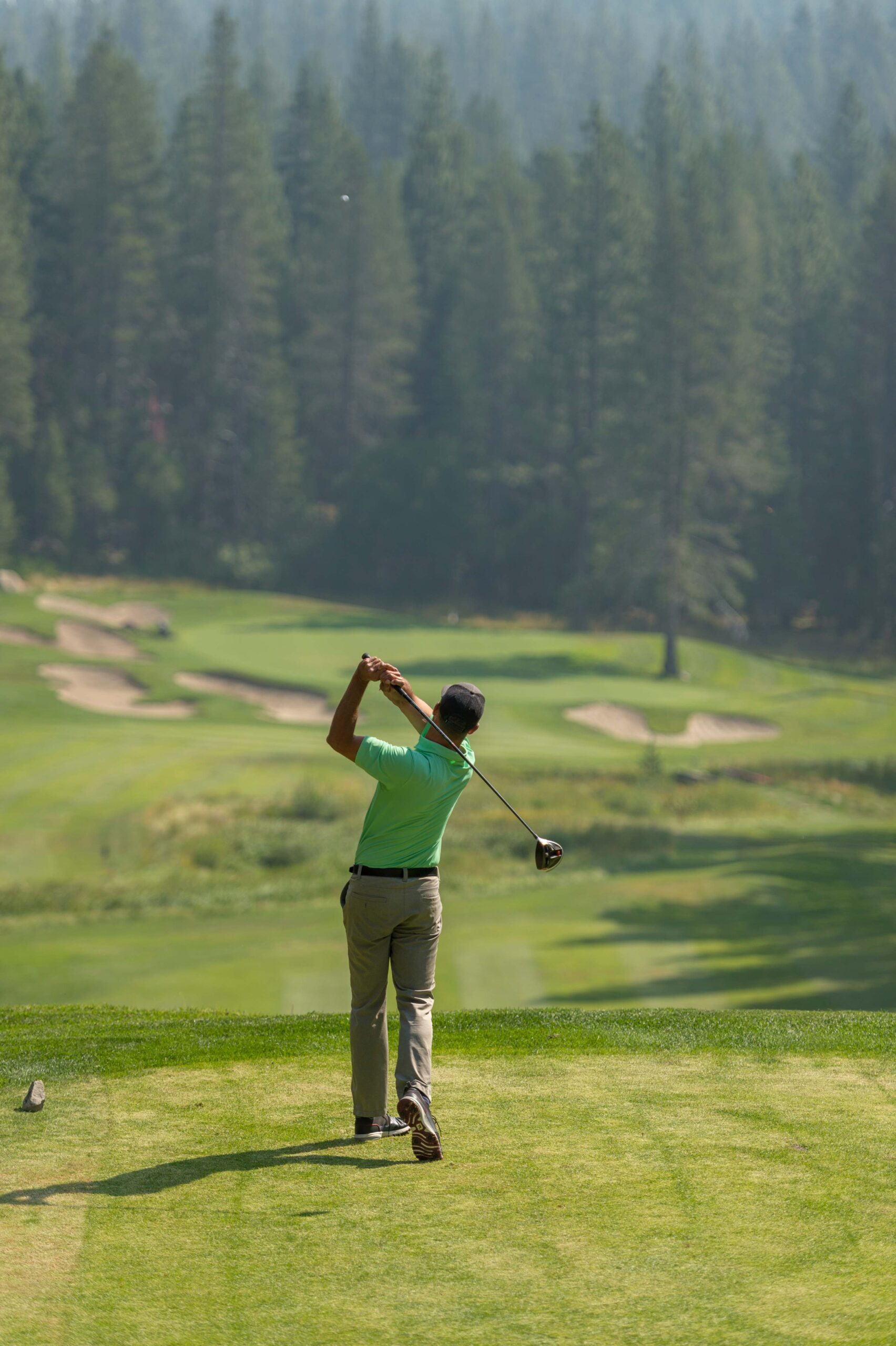 Golfer swings at a scenic course near a Truckee vacation rental, surrounded by lush greenery and tall trees.