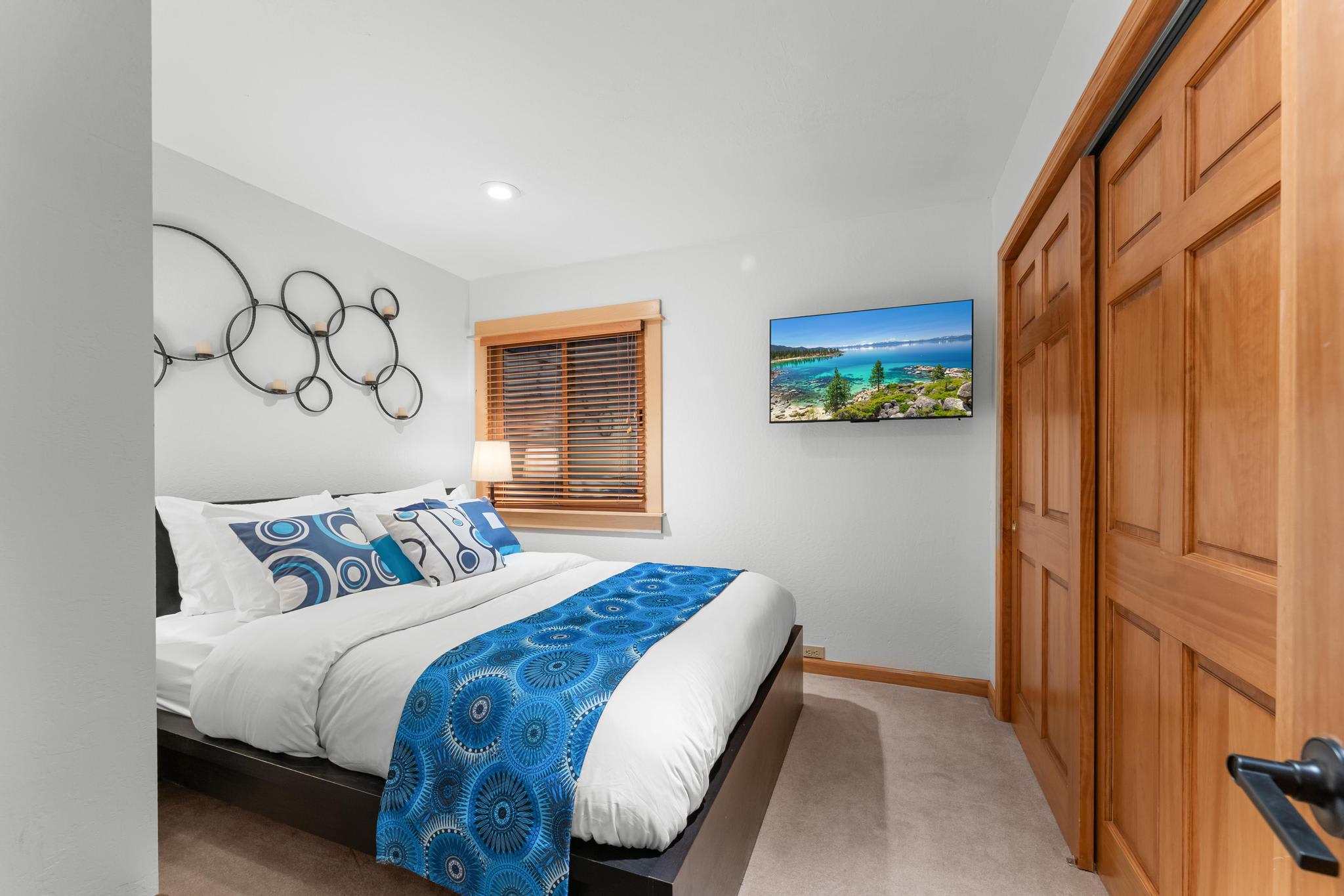Cozy bedroom in a Truckee vacation rental with modern decor, blue accents, and a scenic landscape on the TV.