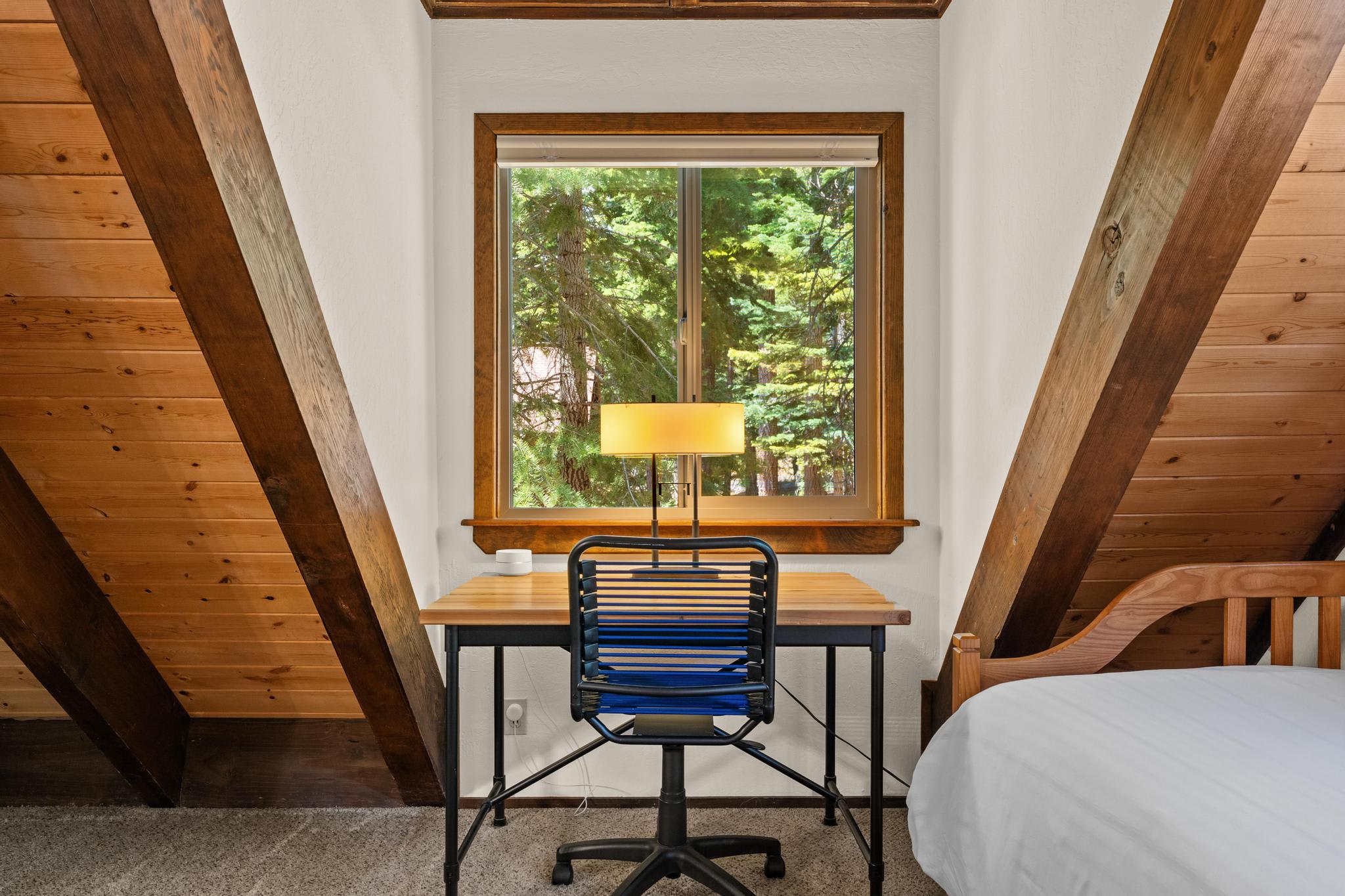Cozy Tahoe Vista vacation rental with wooden beams, a desk by the window, chair, and bed, nestled in forest.