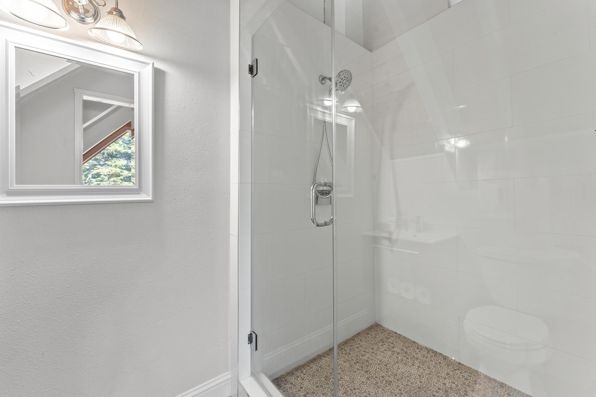 Modern glass shower in Tahoe Vista vacation rental, featuring a sleek design with a large mirror and light fixture.