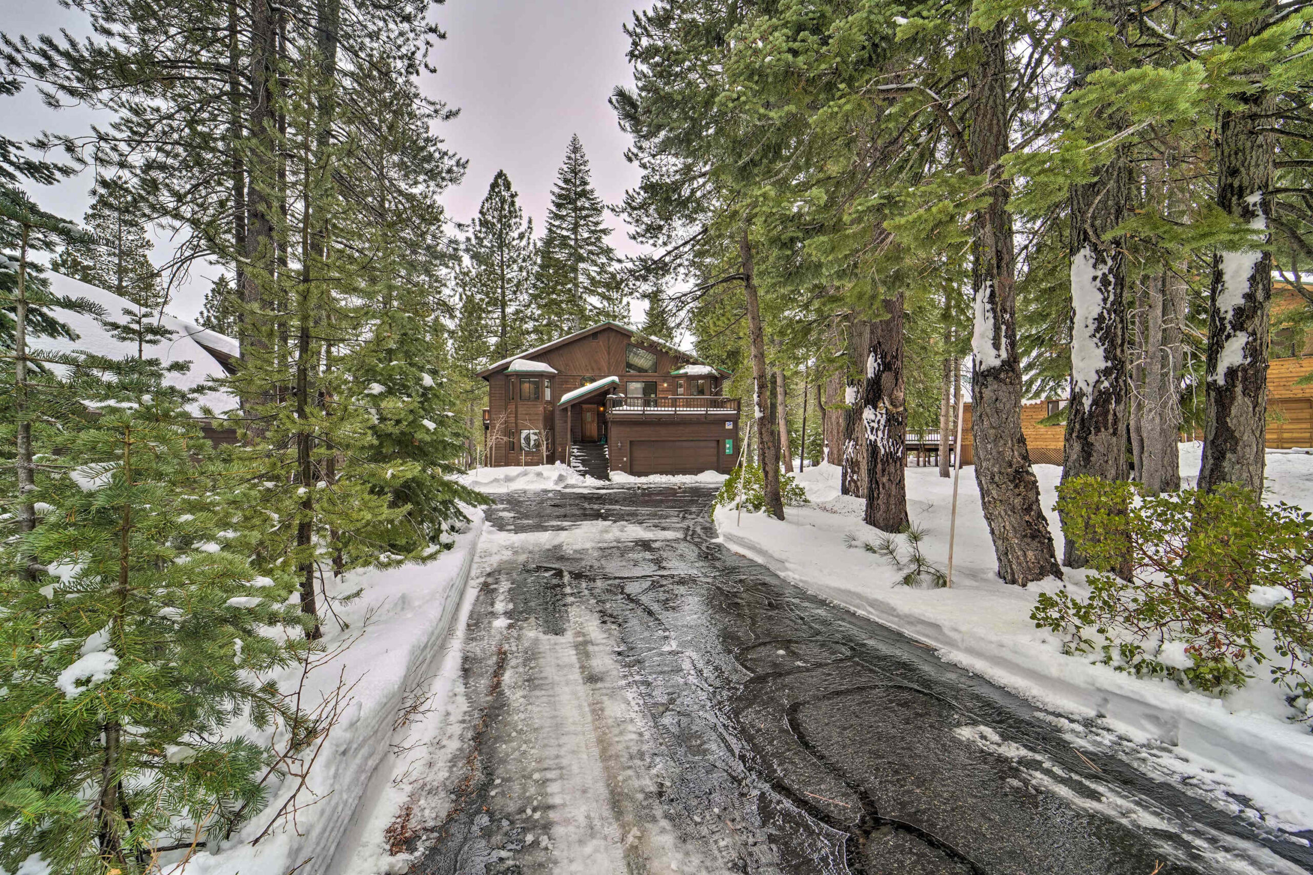 Snowy scene of a cozy vacation rental cabin surrounded by pines in Truckee, with a tree-lined driveway.