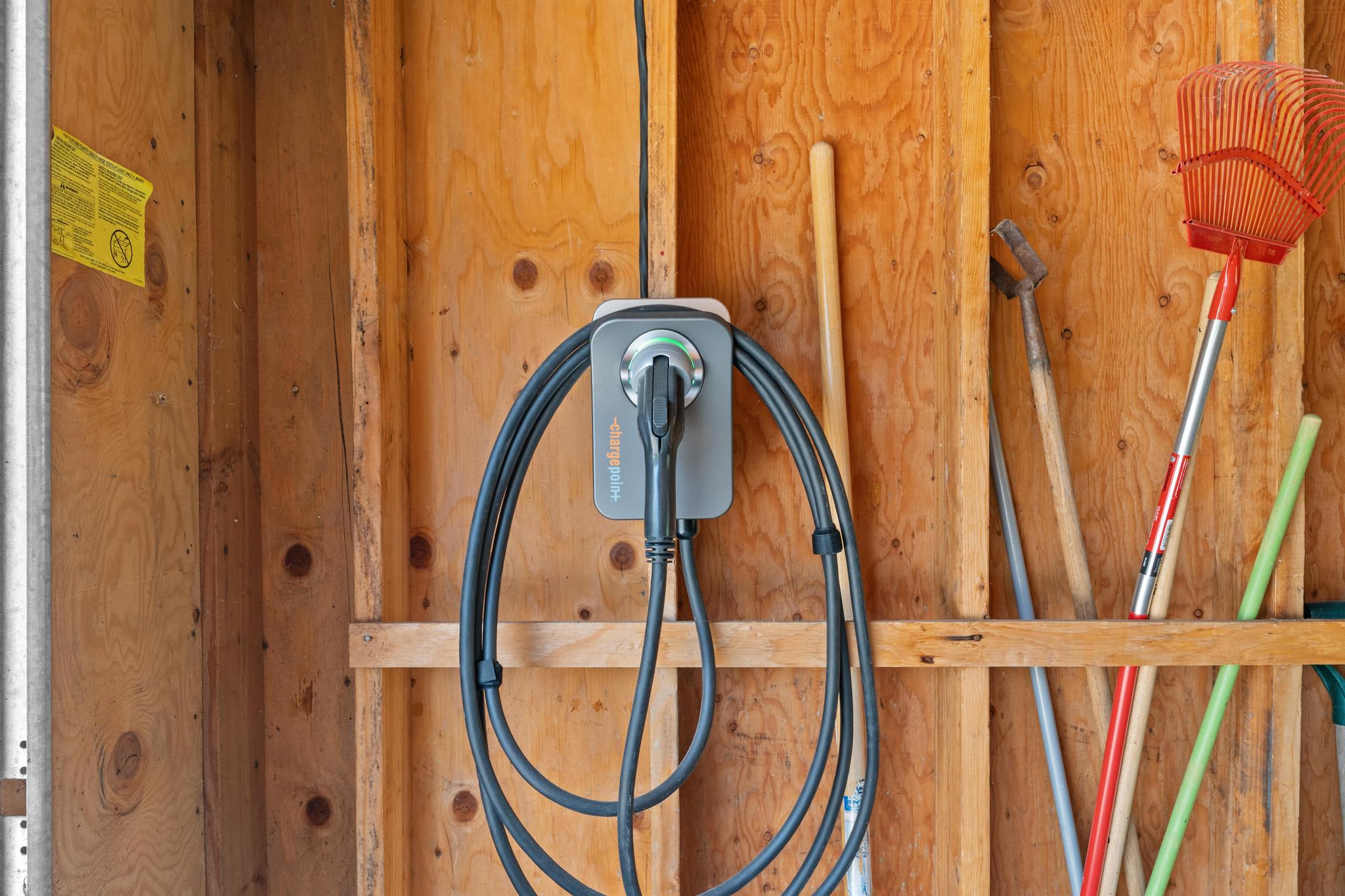 Electric vehicle charger in a Tahoe Vista vacation rental garage, surrounded by wooden walls and garden tools.