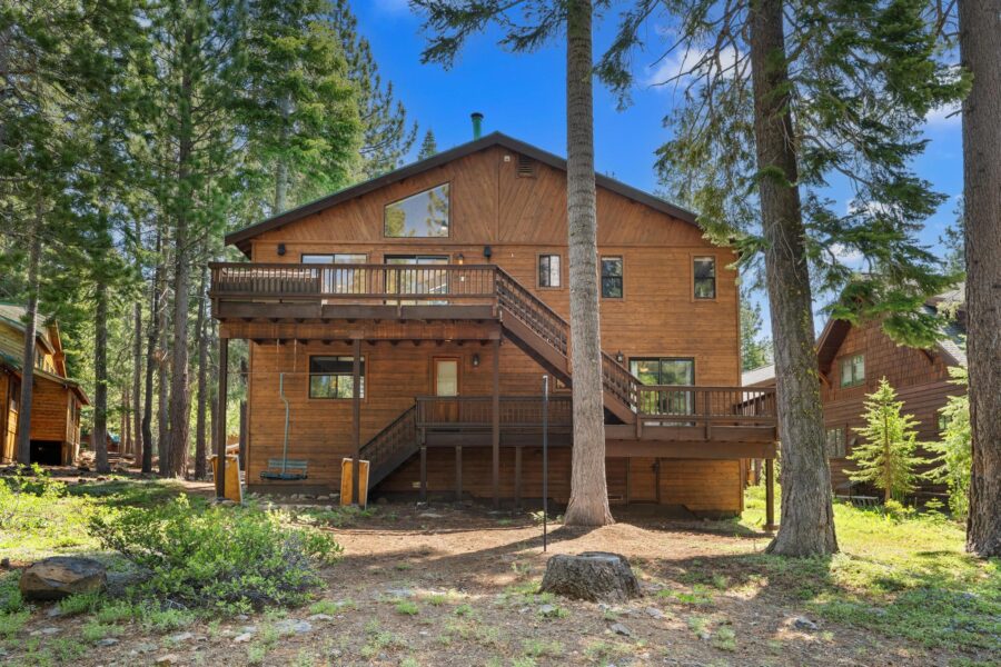 Wooden cabin-style vacation rental in Truckee, surrounded by tall trees and a clear blue sky.