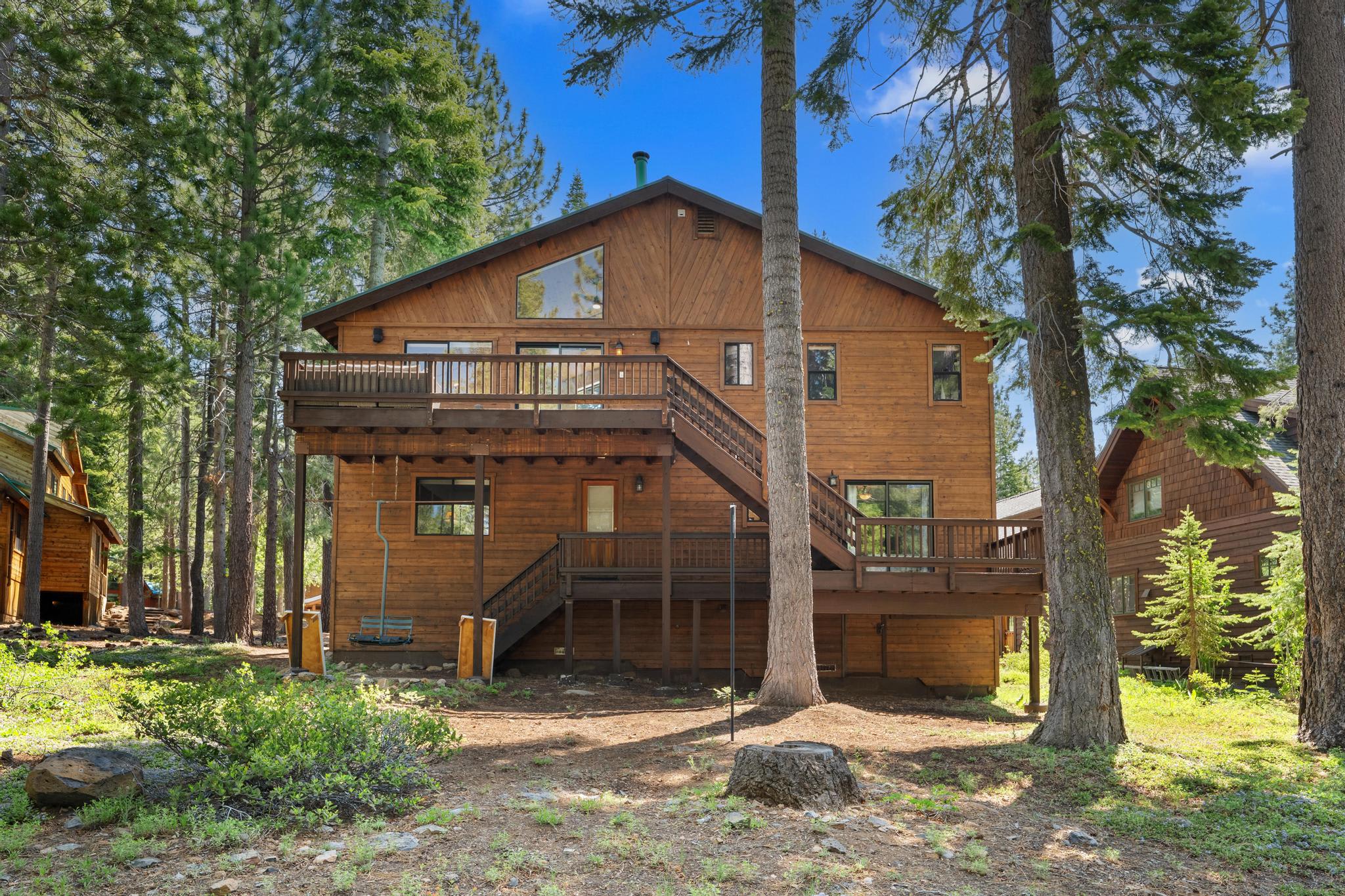 Wooden cabin-style vacation rental in Truckee, surrounded by tall trees and a clear blue sky.
