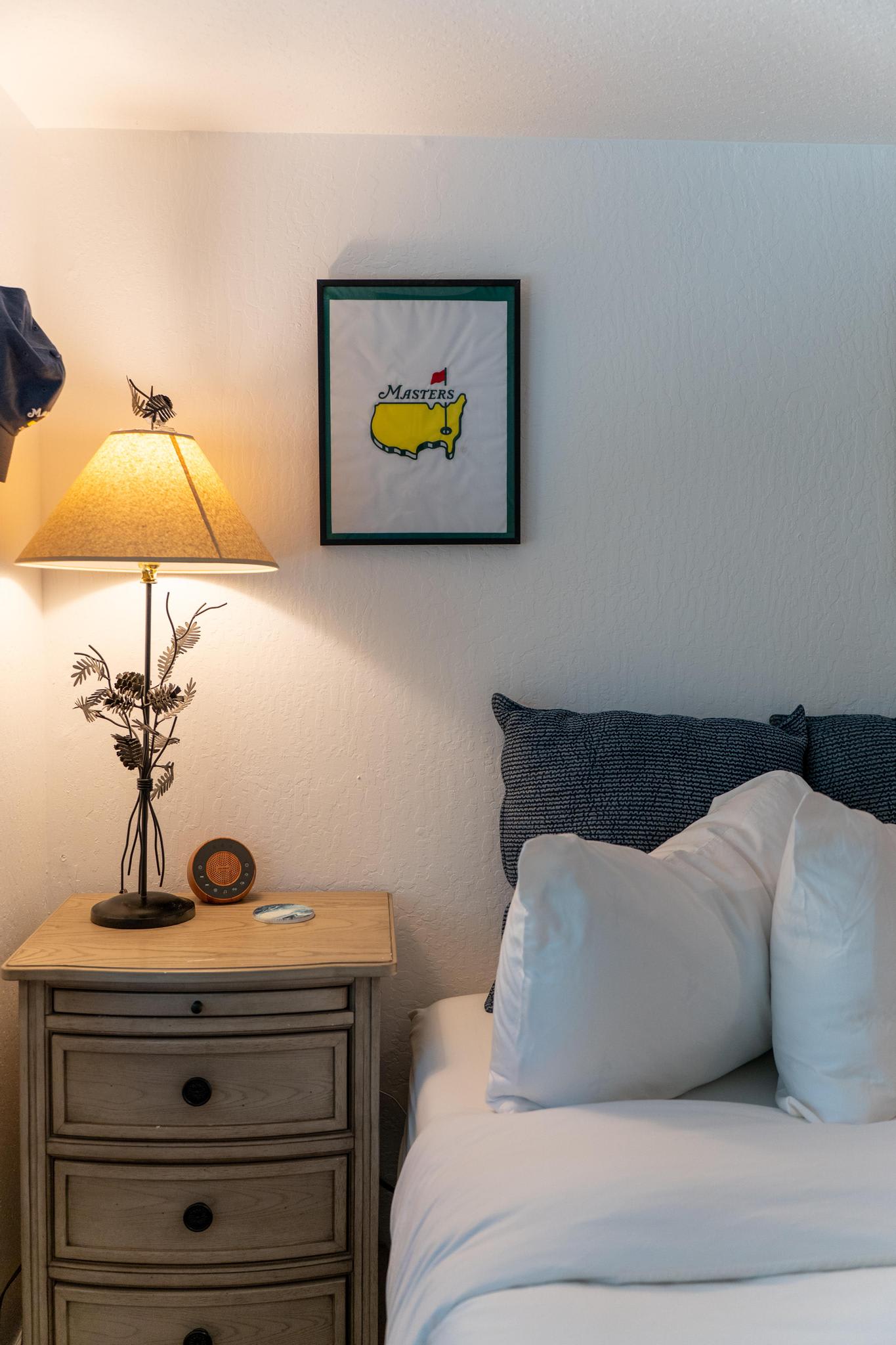 Cozy bedroom in a Truckee vacation rental with a framed Masters print, lamp, and a small wooden nightstand.