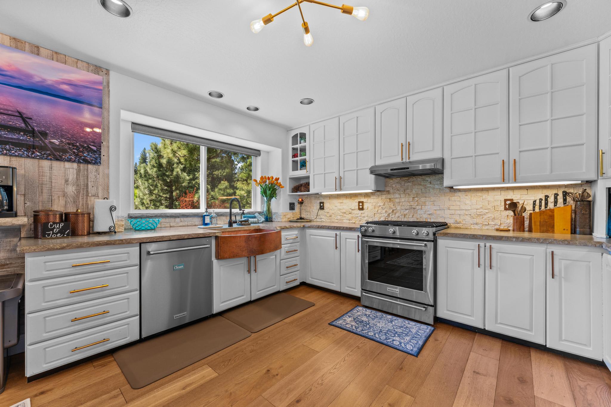 Modern kitchen in Truckee vacation rental with white cabinets, copper sink, stainless appliances, and woodland view.