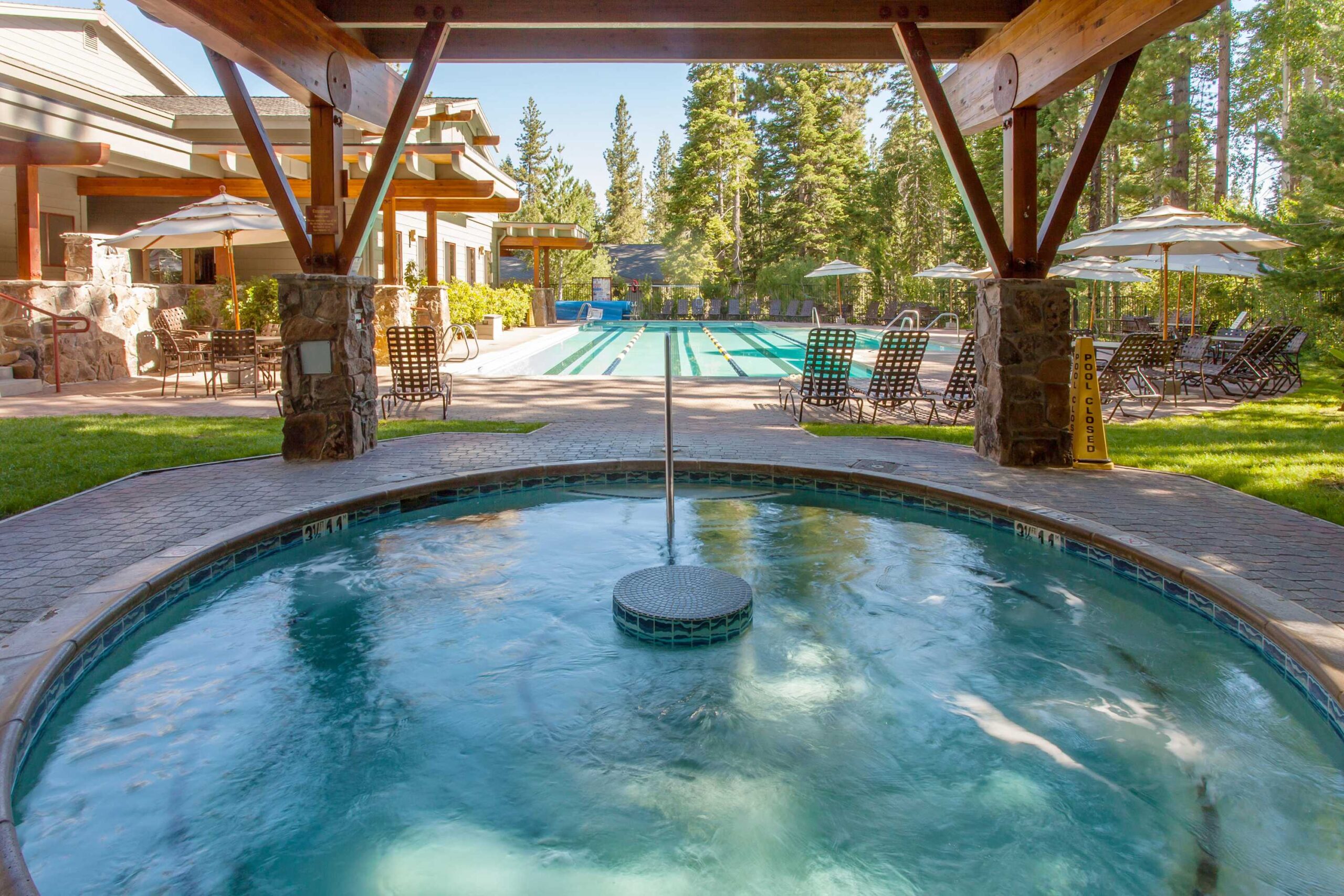 Outdoor pool area at a Truckee vacation rental with hot tub, loungers, and shaded seating amidst tall trees.