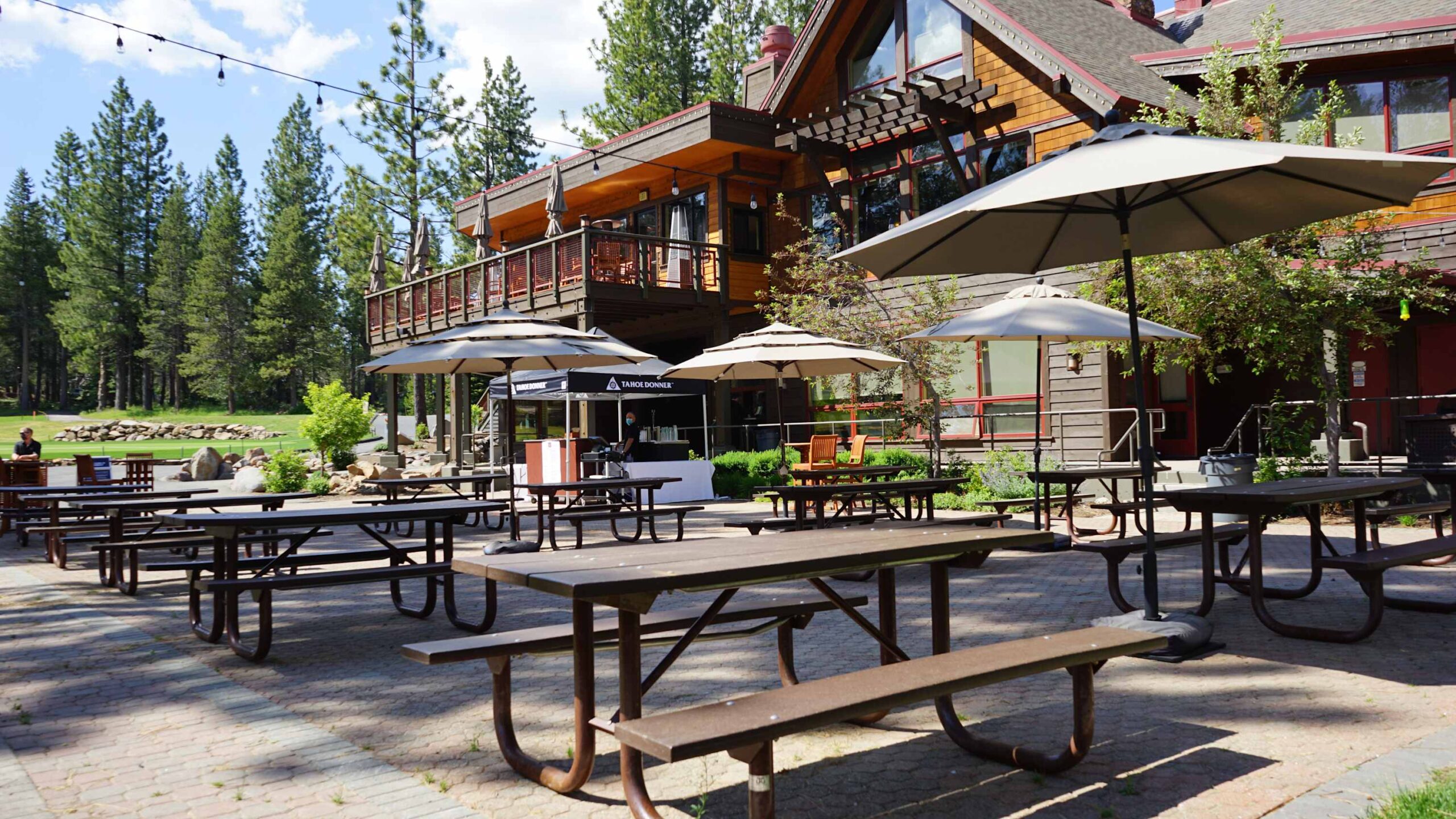 Outdoor patio with picnic tables and umbrellas at a vacation rental in Truckee, surrounded by tall pine trees.