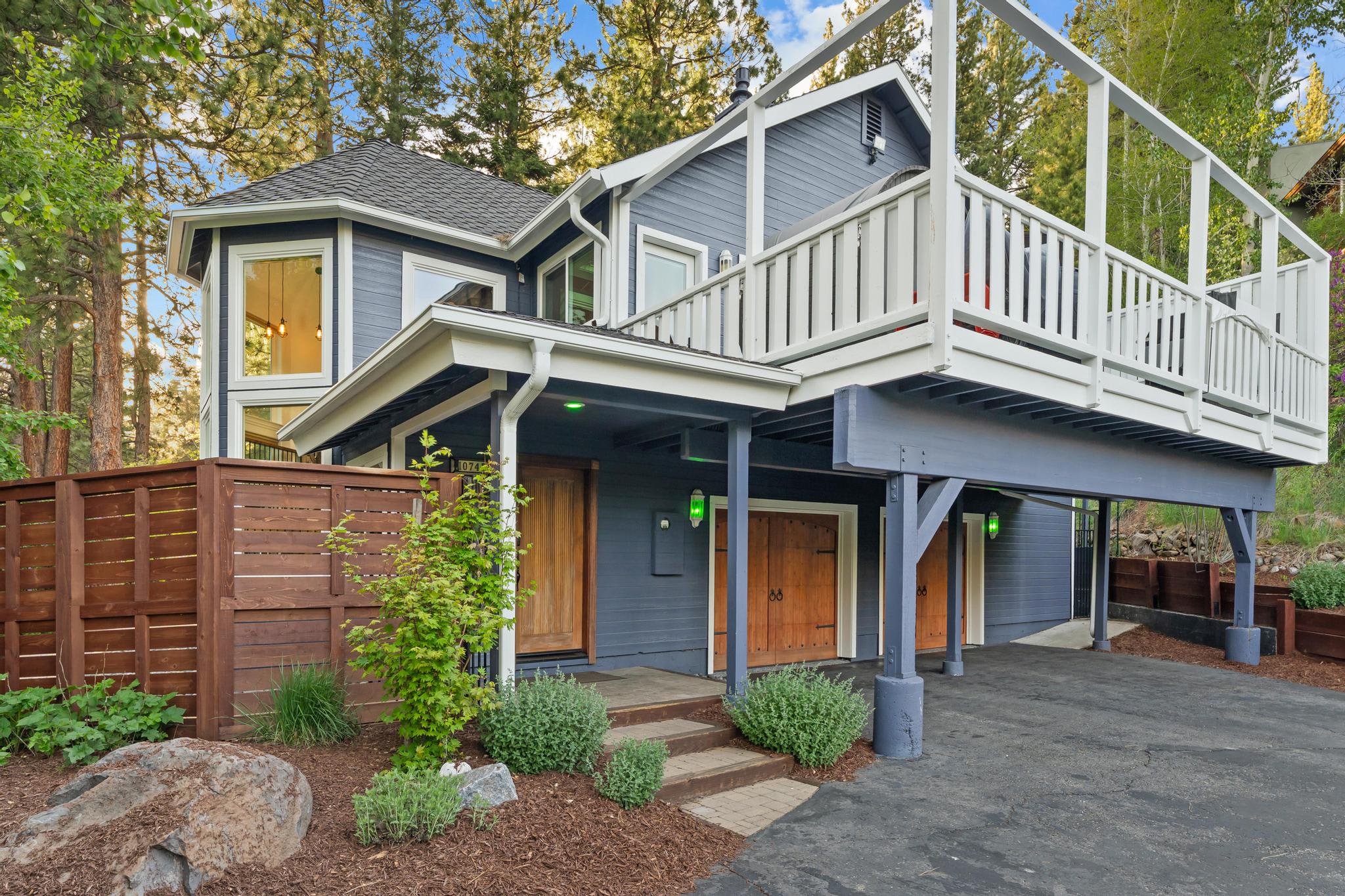 Blue two-story vacation rental in Truckee, surrounded by trees, featuring a large balcony and wooden doors.