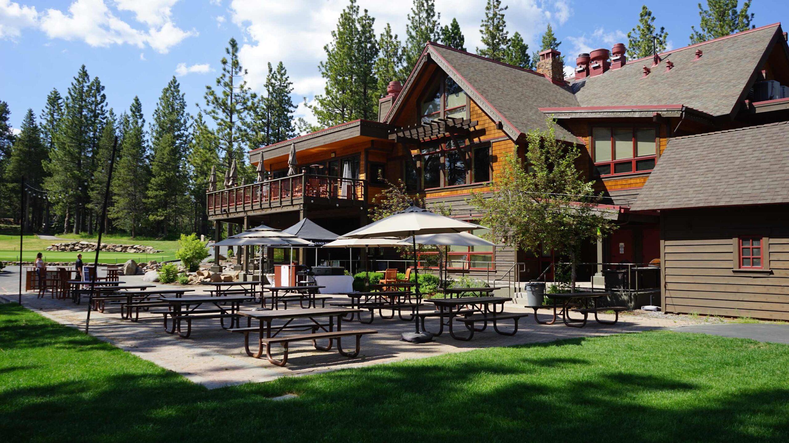Truckee vacation rental with a large wood cabin, outdoor seating, and surrounded by tall pine trees under a blue sky.