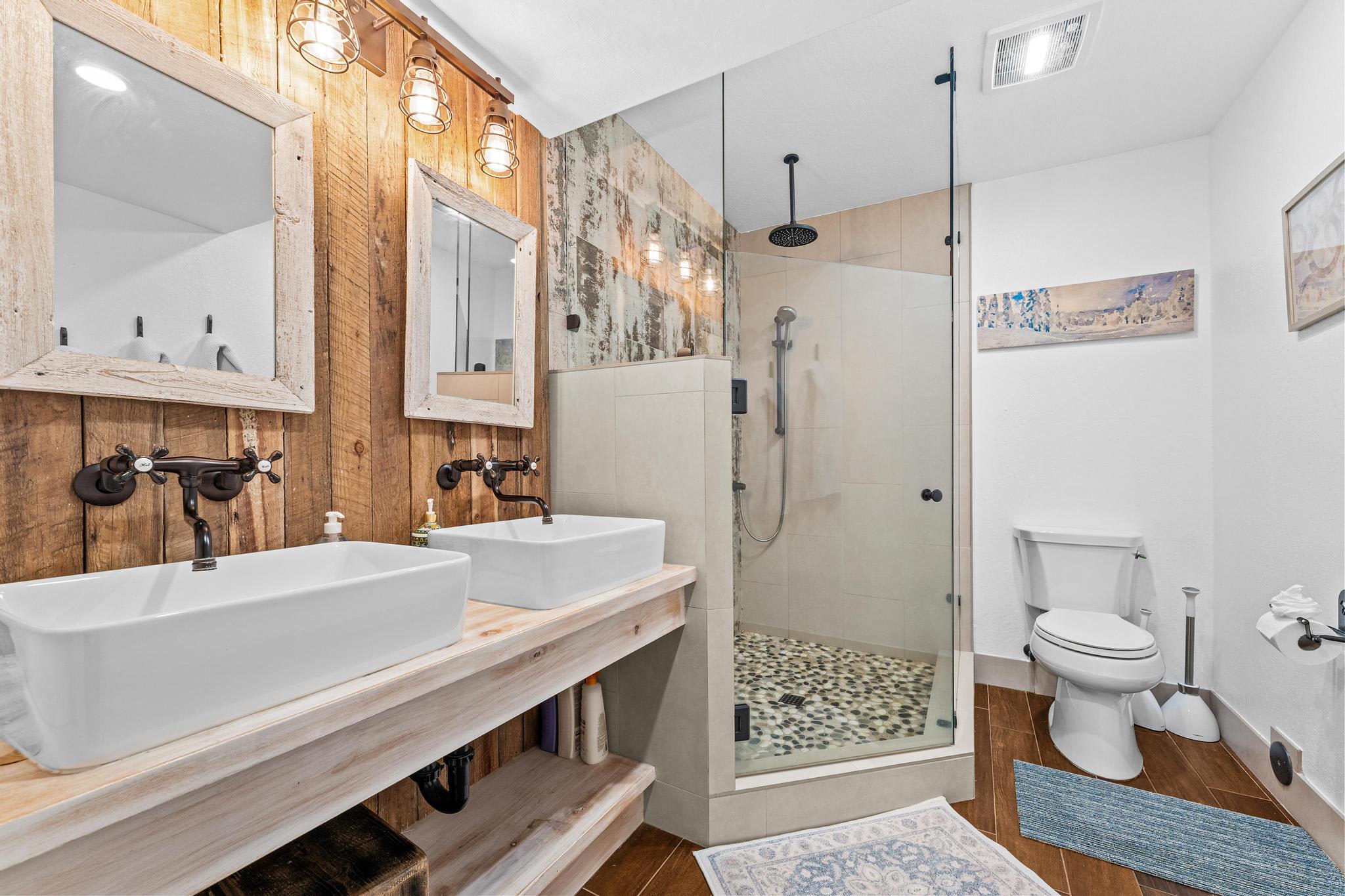 Rustic bathroom in a Truckee vacation rental, featuring dual sinks, wood accents, and a glass shower with pebble floor.
