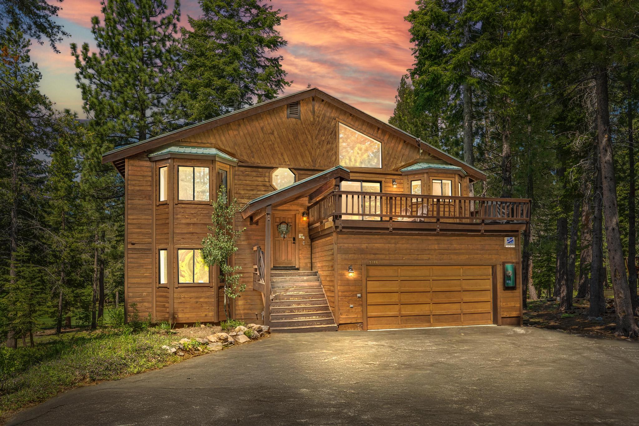 Wooden vacation rental in Truckee surrounded by pine trees, featuring a large balcony and a sunset sky backdrop.