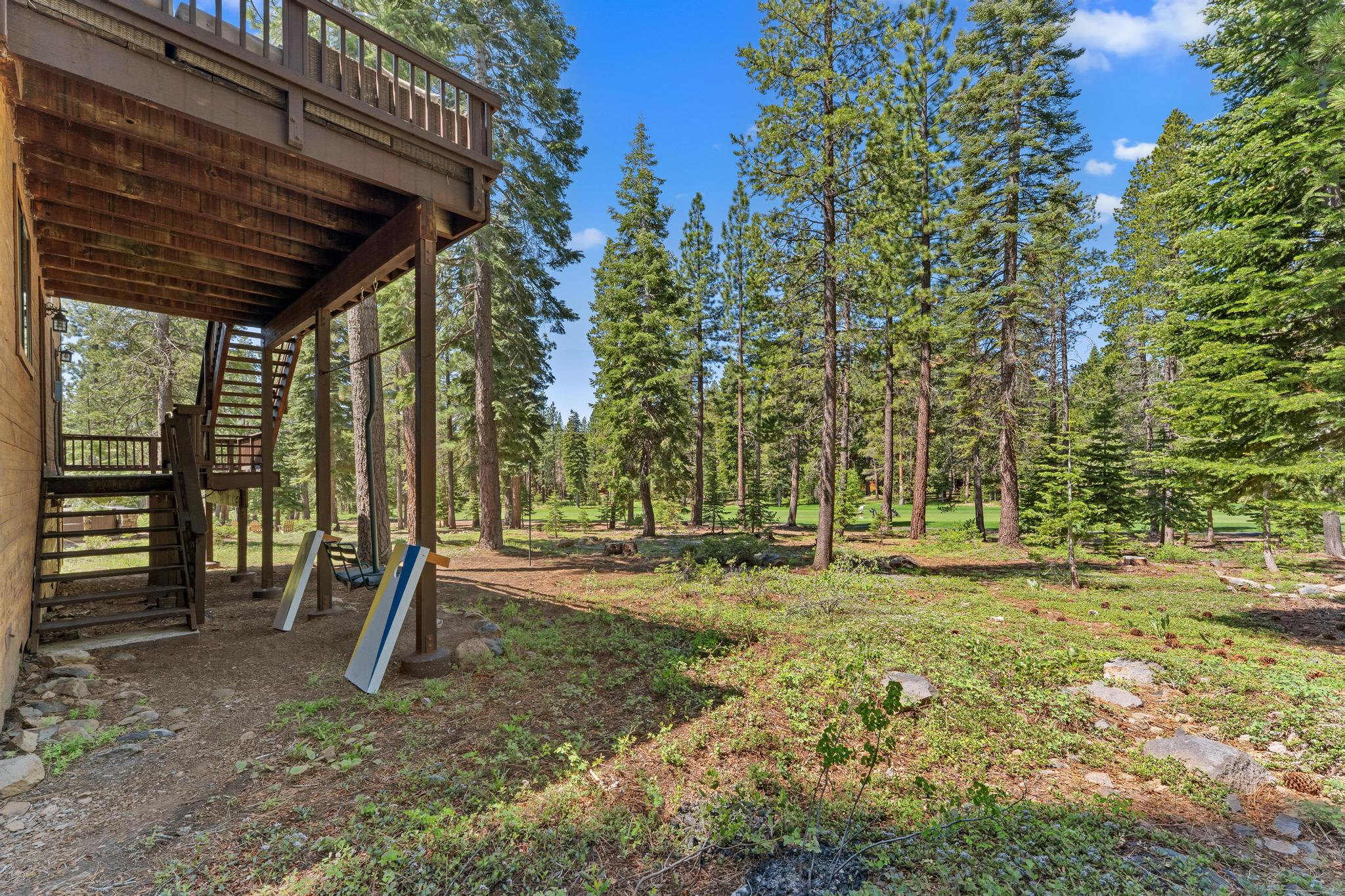 Truckee vacation rental with forest views, featuring a wooden deck and stairs amidst towering pine trees.