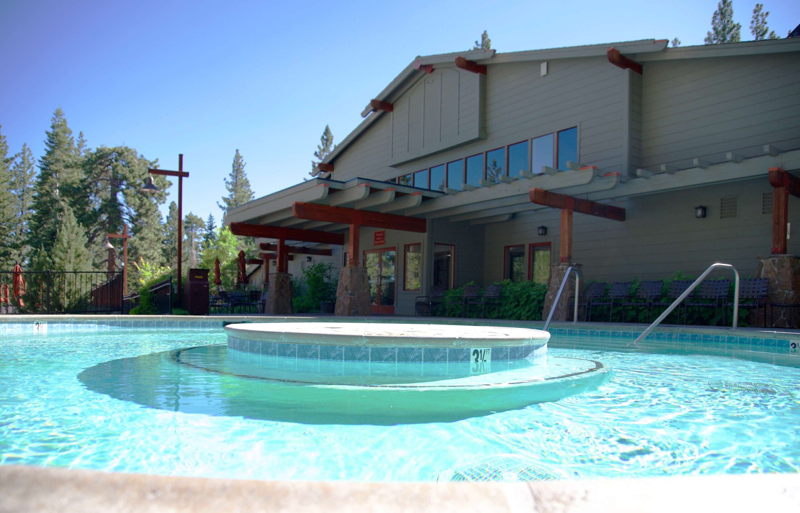 Outdoor pool at a vacation rental in Truckee surrounded by tall trees and a rustic building under a clear blue sky.