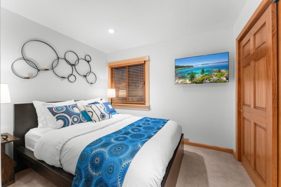 Modern bedroom in a Truckee vacation rental with a cozy bed, abstract wall art, and scenic landscape on TV.
