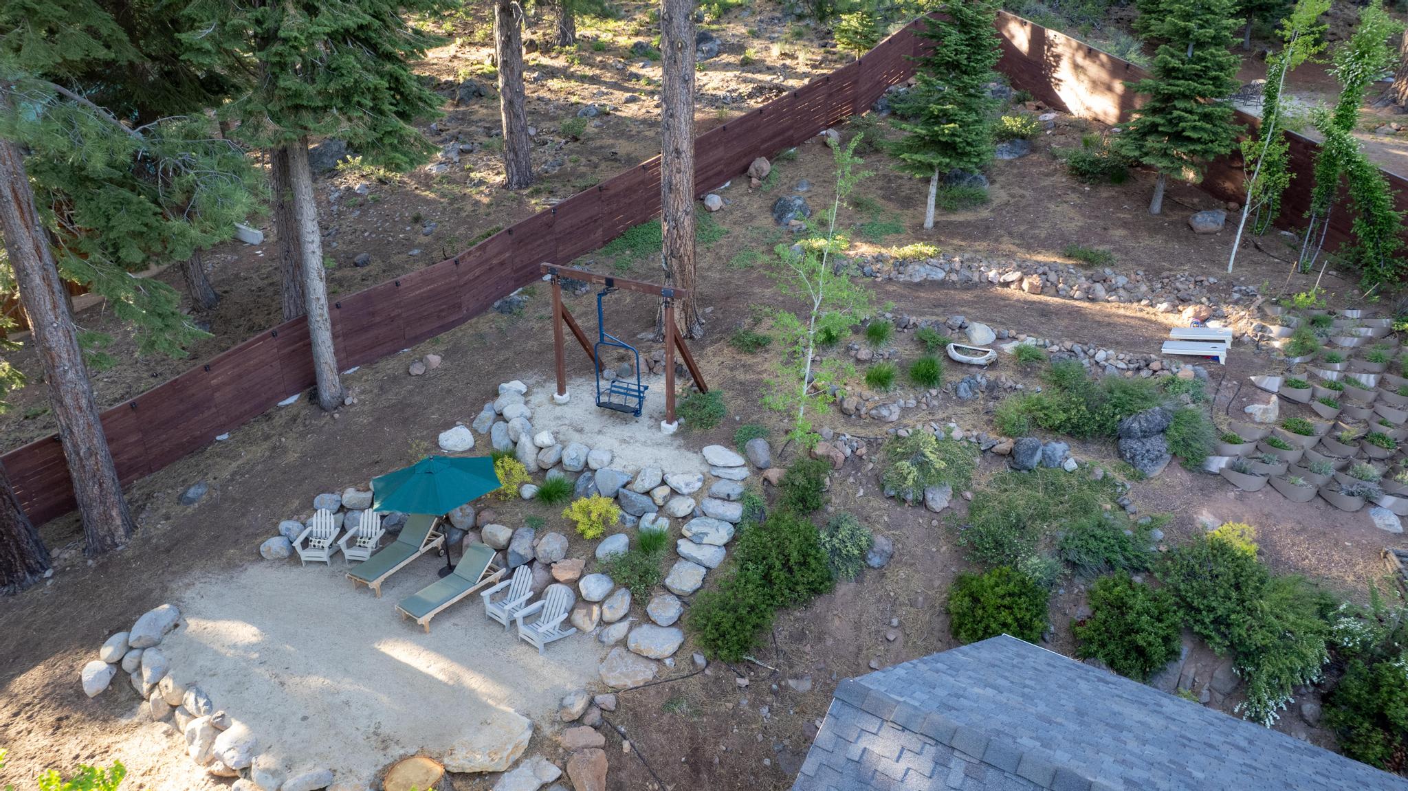 Outdoor seating at a Truckee vacation rental with chairs, loungers, and a swing amidst trees and rock landscaping.