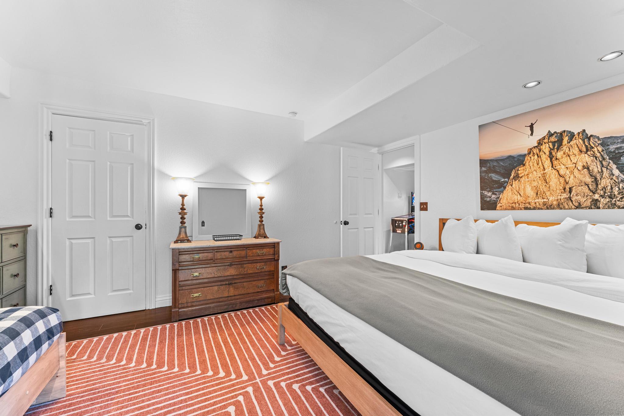 Cozy bedroom in Truckee vacation rental with king bed, orange patterned rug, wooden dresser under bright lamps.
