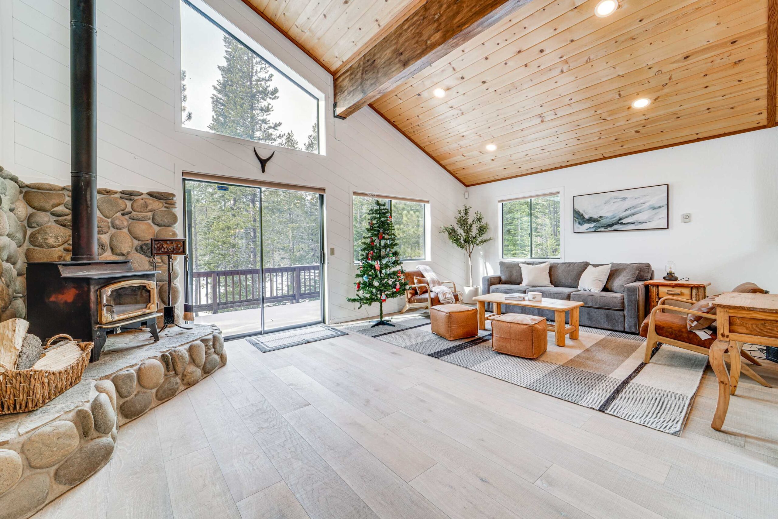 Spacious Truckee vacation rental with rustic decor, stone fireplace, and large windows overlooking a snowy forest.