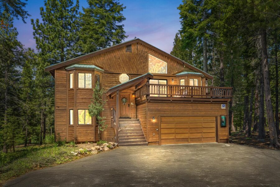 Wooden vacation rental cabin in Truckee, nestled among tall trees, featuring a large driveway and balcony.