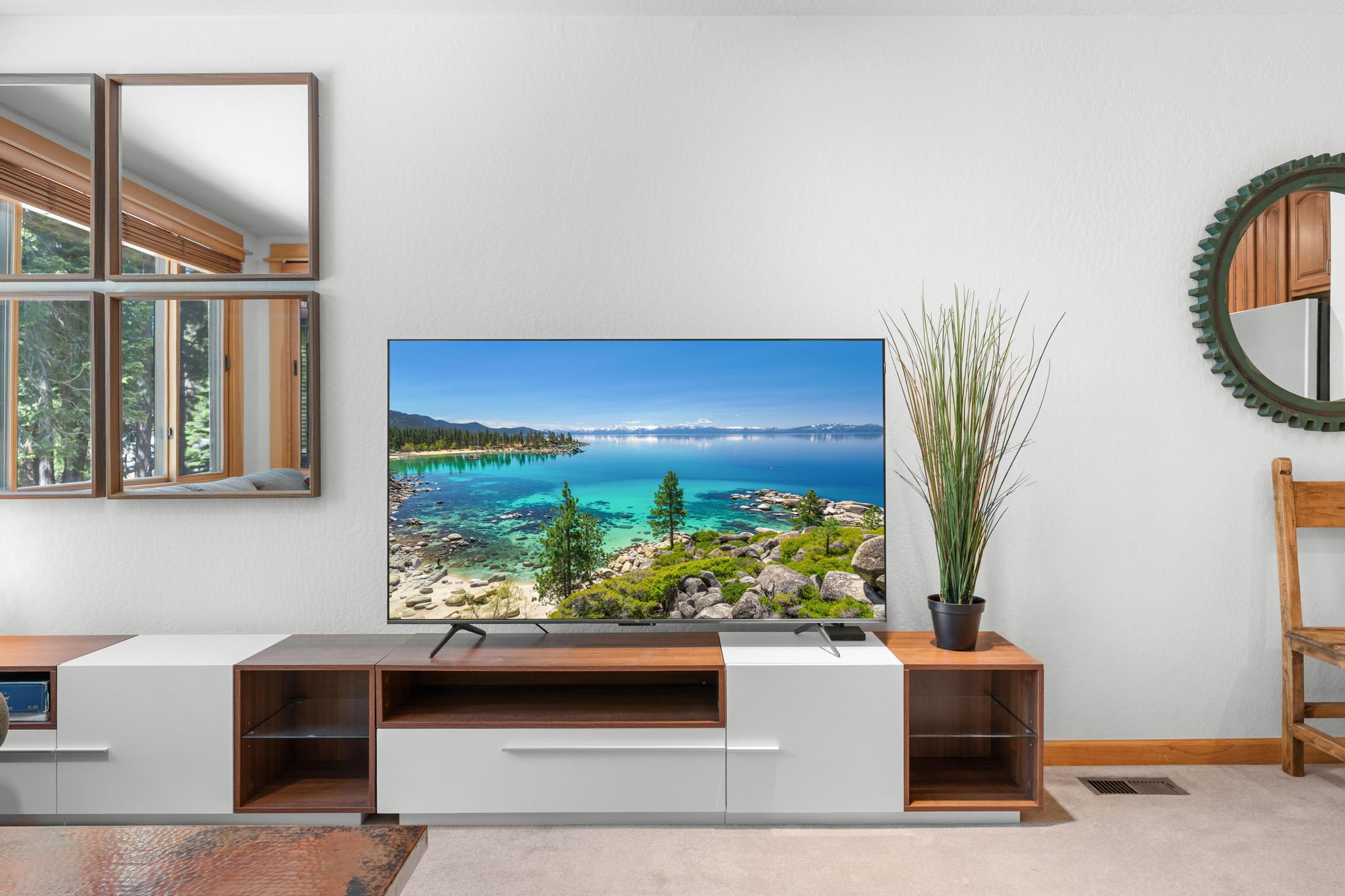 Modern living room in a Truckee vacation rental featuring a large TV, scenic view, wooden accents, and mirrors on the wall.