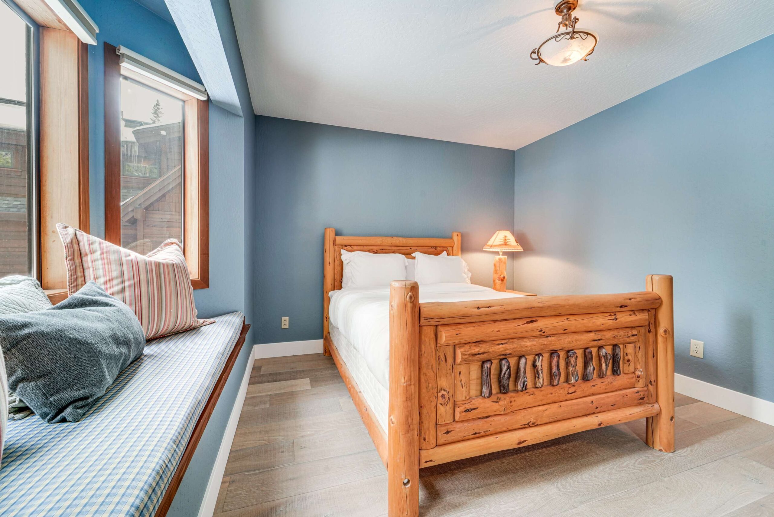 Cozy bedroom in a Truckee vacation rental with wood bed, blue walls, and a window seat with striped pillows.