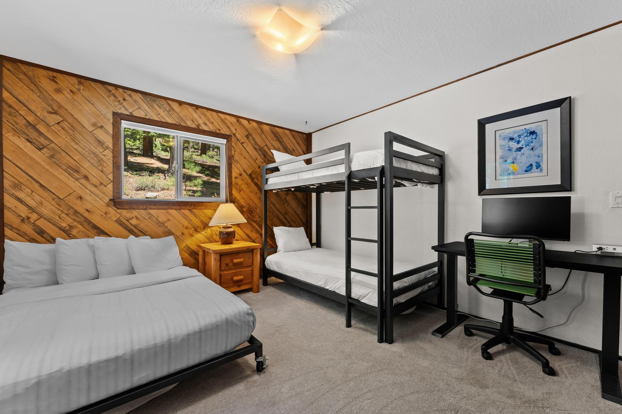 Cozy vacation rental room in Tahoe Vista with a bed, bunk bed, desk, chair, lamp, and wooden accent wall.