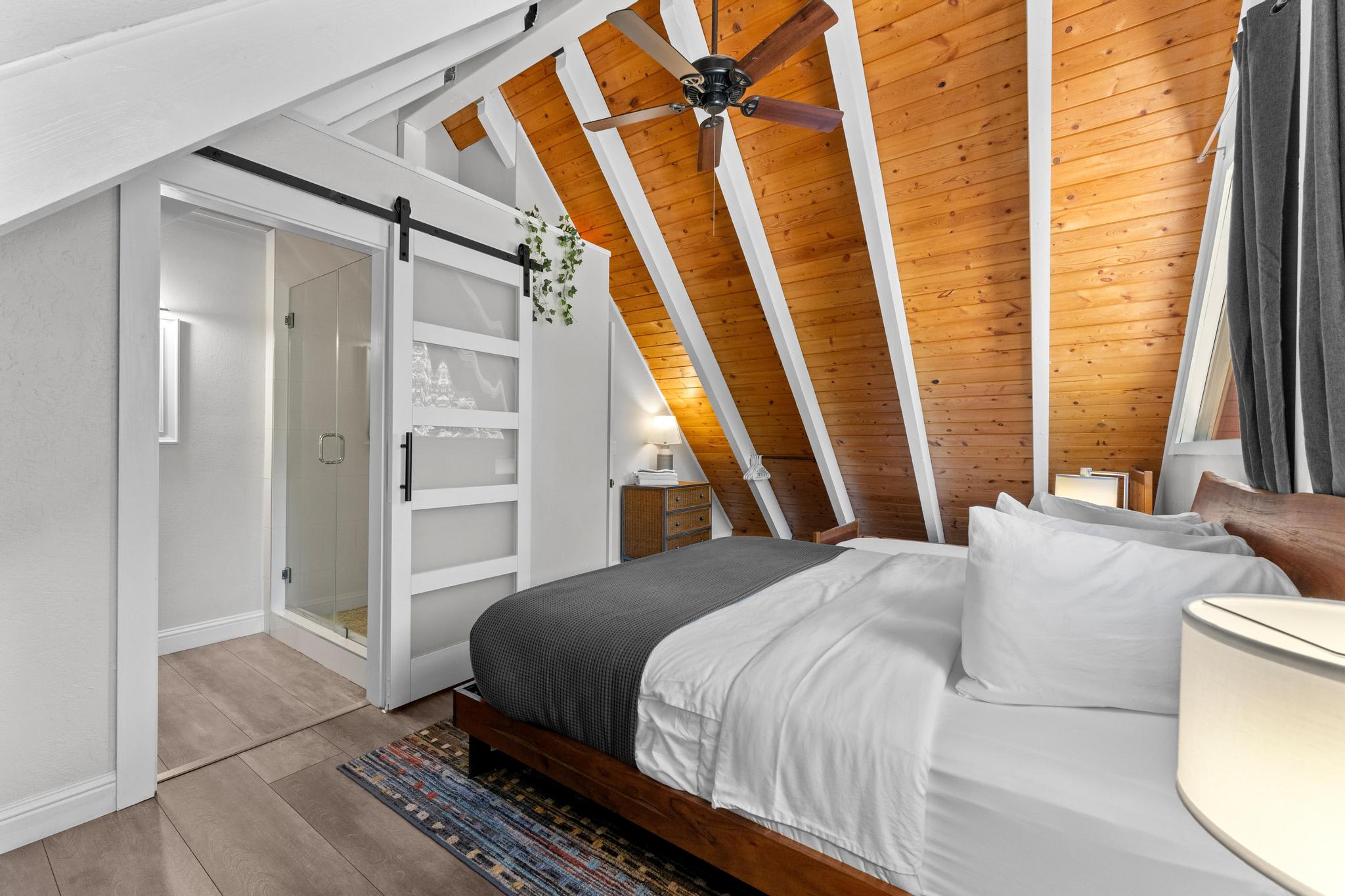 Cozy bedroom in a Tahoe Vista vacation rental with wooden ceilings, modern decor, and a sliding bathroom door.