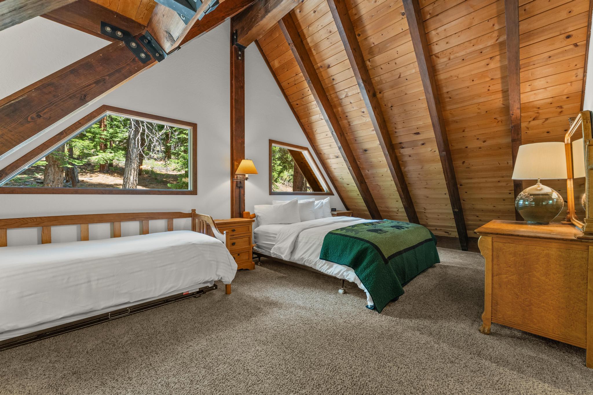 A cozy attic bedroom in a Tahoe Vista vacation rental with wooden beams, two beds, and forest view windows.
