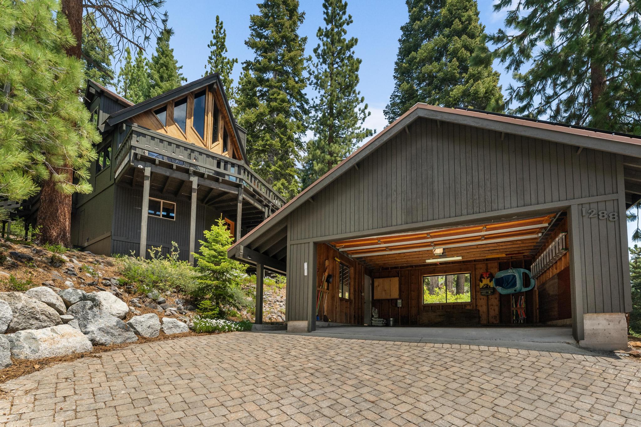 Charming A-frame cabin vacation rental in Tahoe Vista, surrounded by tall pine trees. Spacious driveway and open garage.