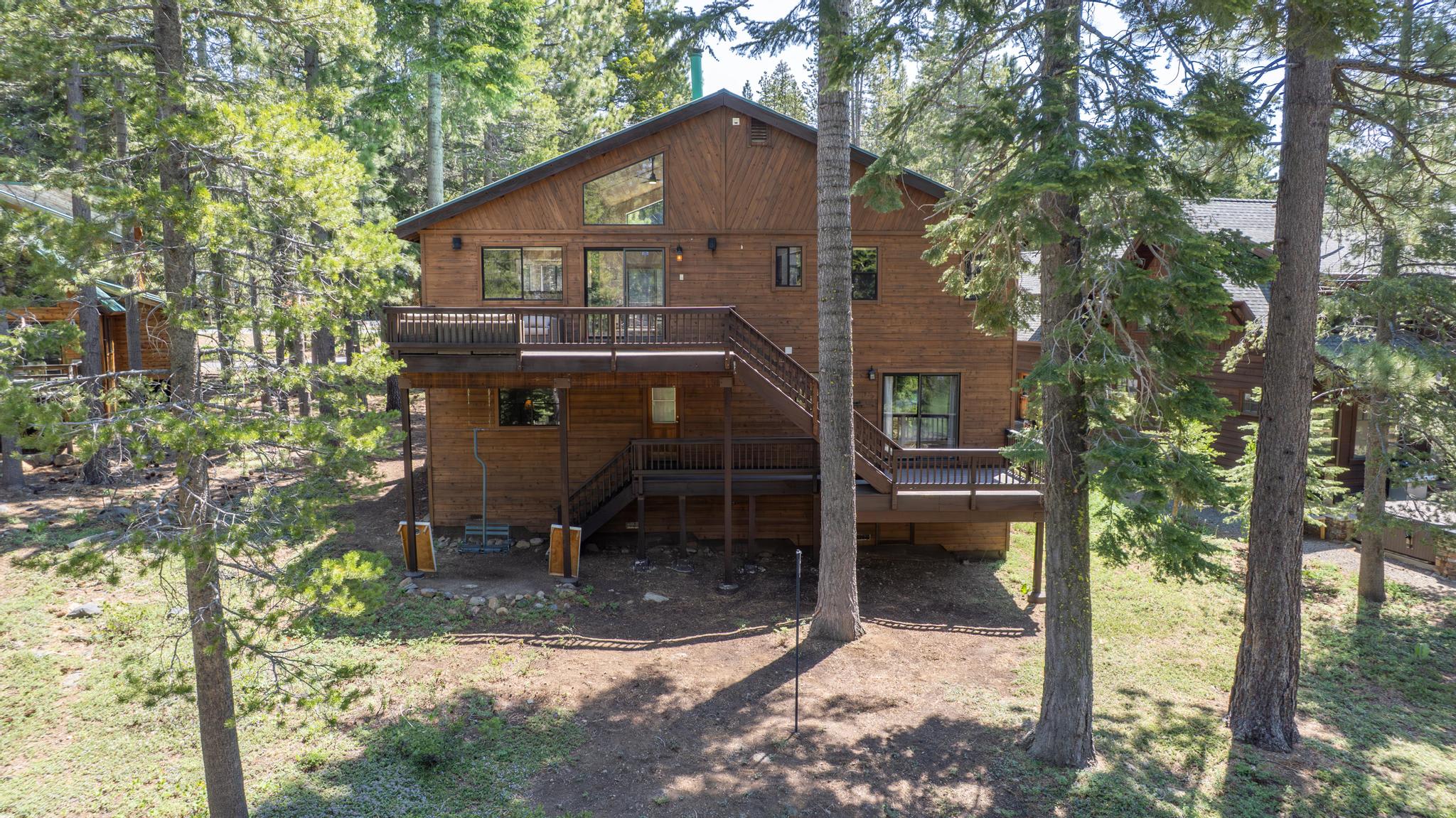 Wooden vacation rental in Truckee, surrounded by tall trees, features a large deck and two-story structure.