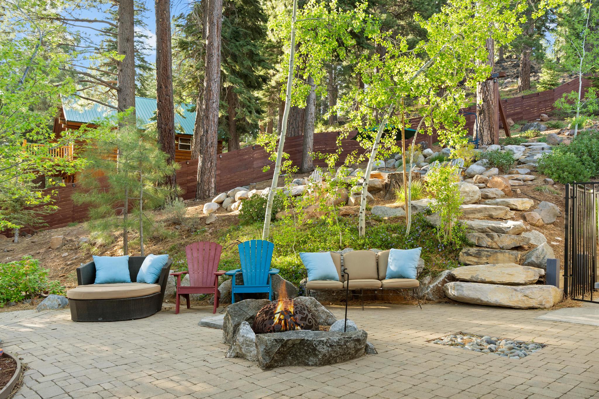 Outdoor seating with Adirondack chairs and fire pit at a Truckee vacation rental, surrounded by trees and rocks.