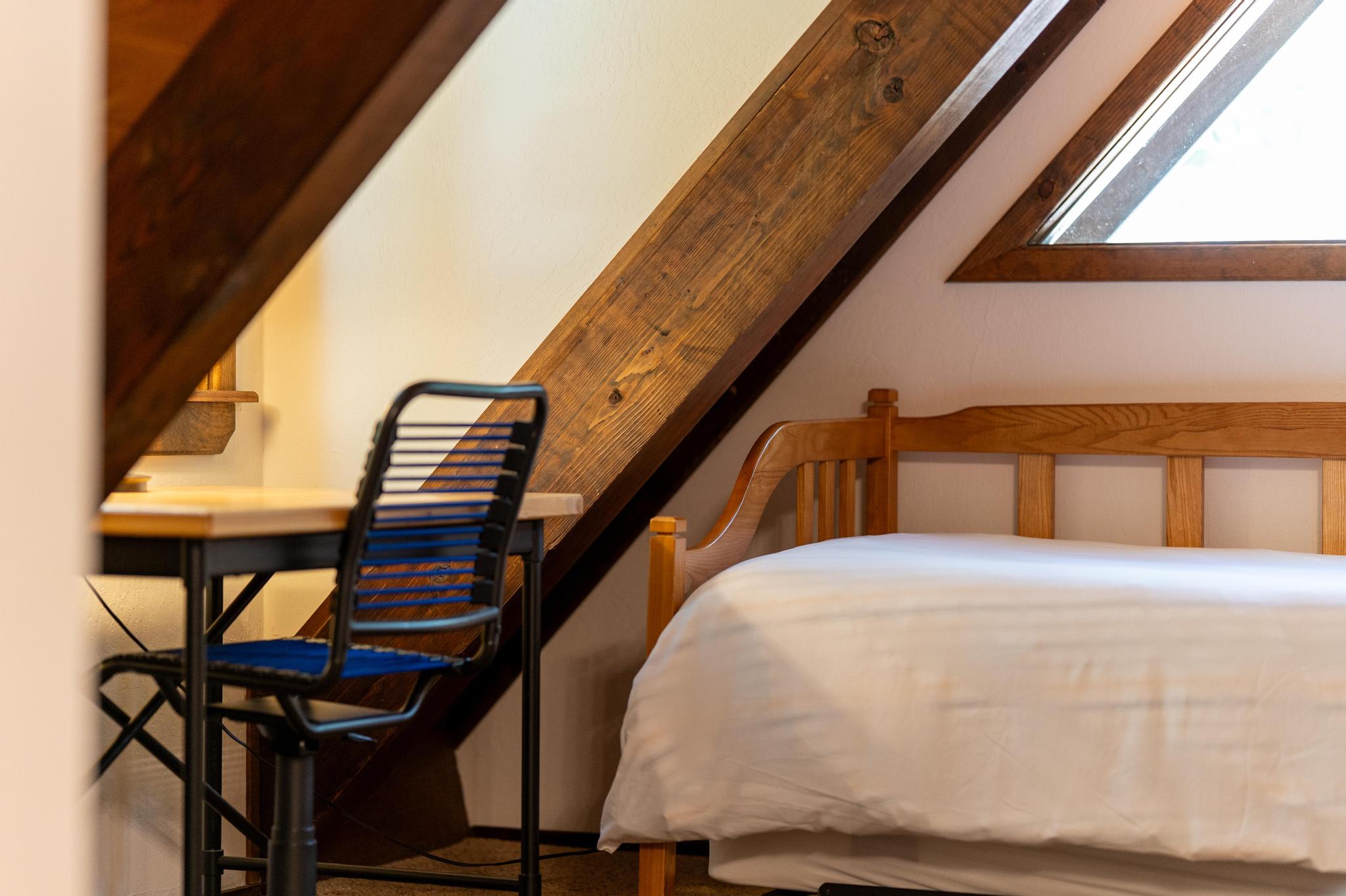 Cozy Tahoe Vista vacation rental loft with sloped wooden ceiling, a comfy bed, small desk, and chair by window.