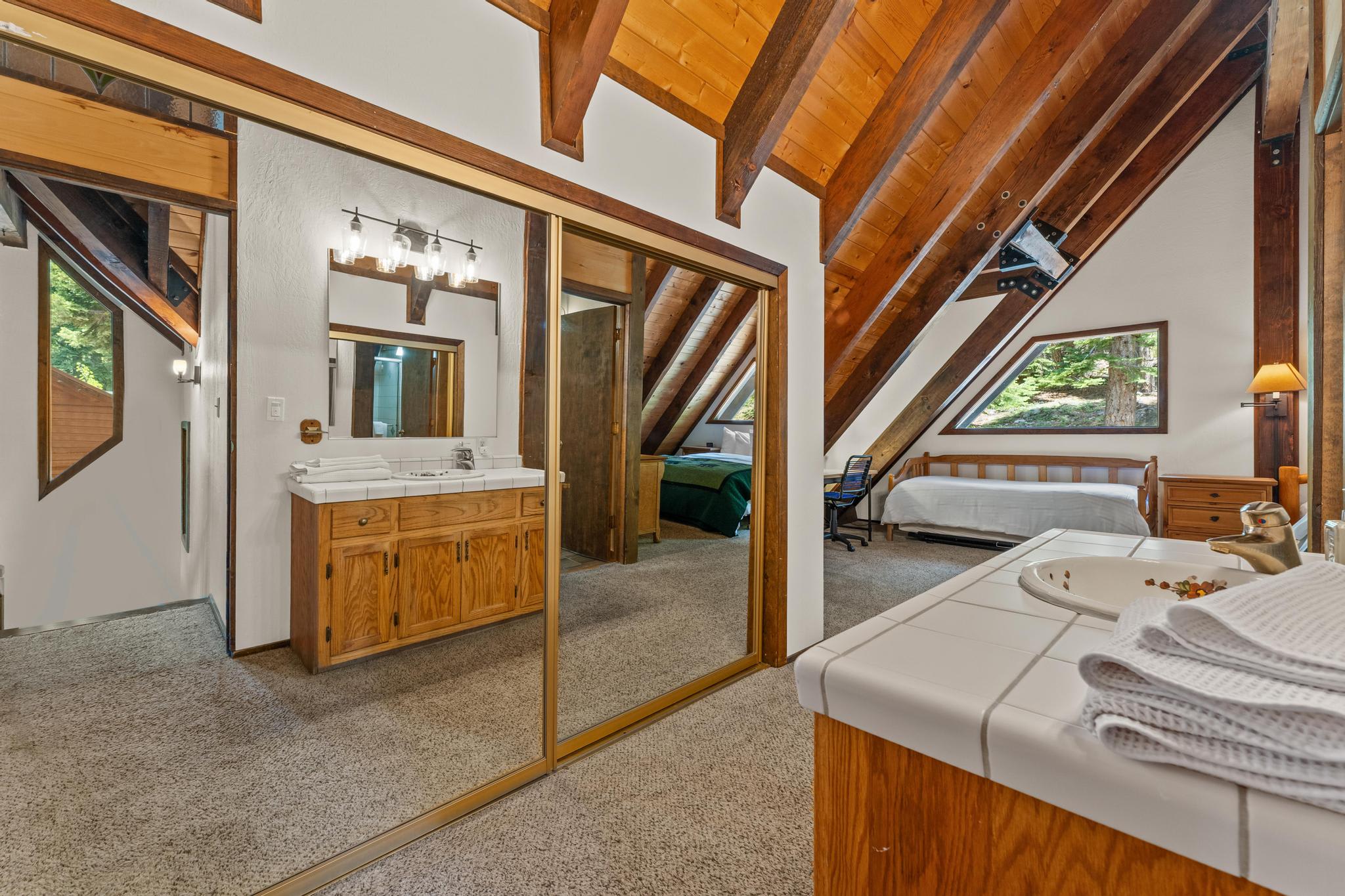 A cozy loft bedroom with wooden beams and a bathroom in a Tahoe Vista vacation rental, featuring a mirrored closet.
