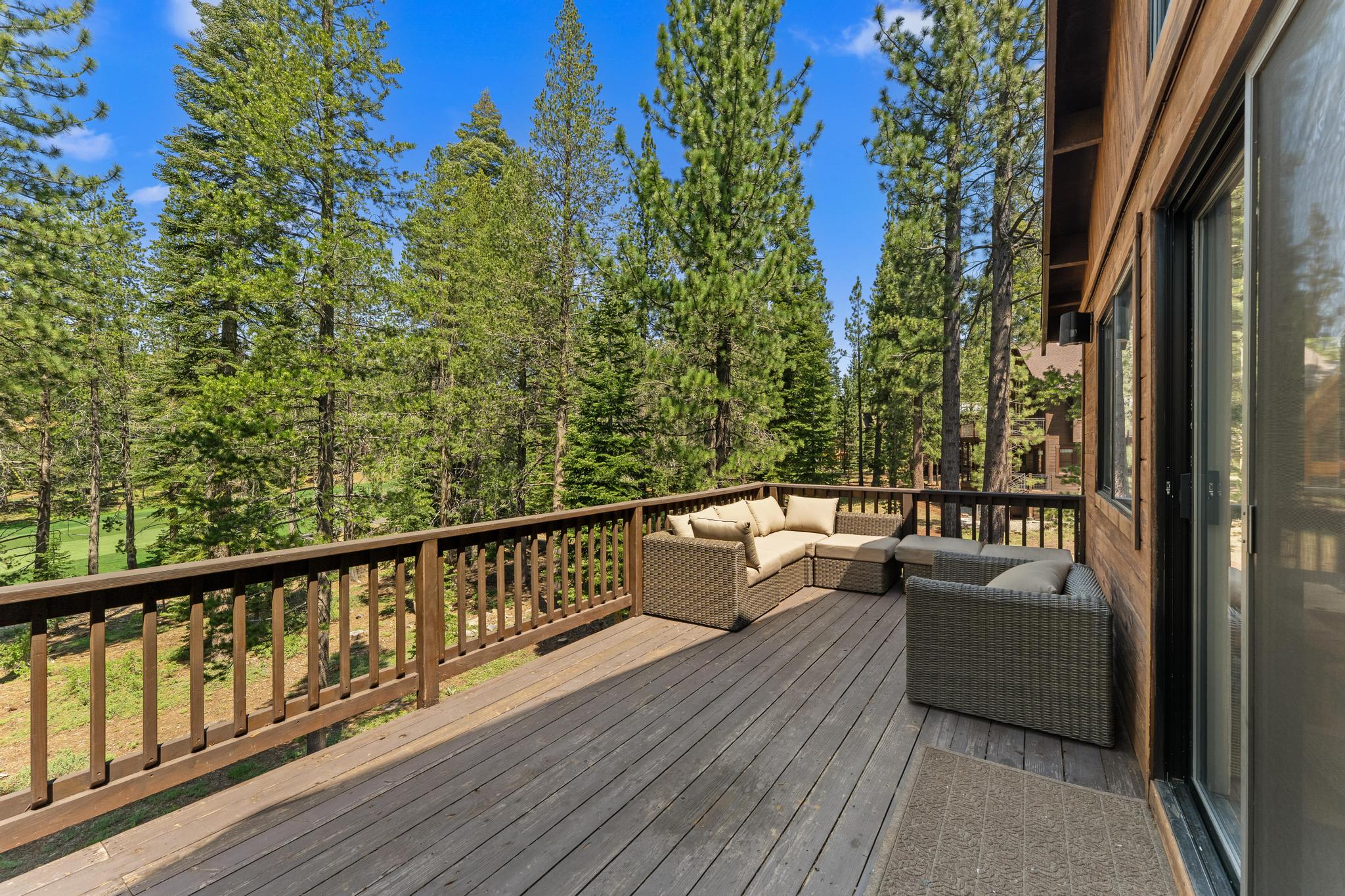 Truckee vacation rental with a wooden deck, seating area, and forest views under a clear blue sky.