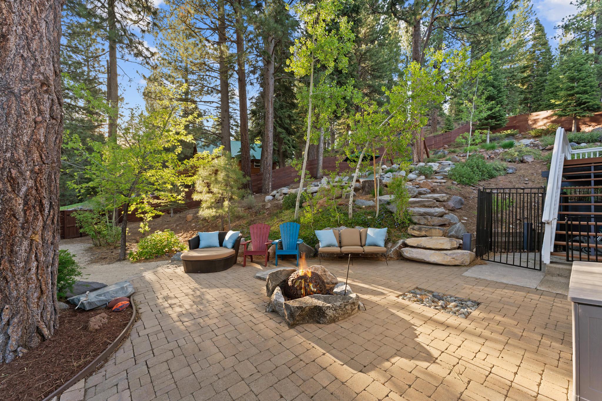 Outdoor patio in Truckee vacation rental with cozy seating, fire pit, and surrounded by tall trees and natural landscaping.