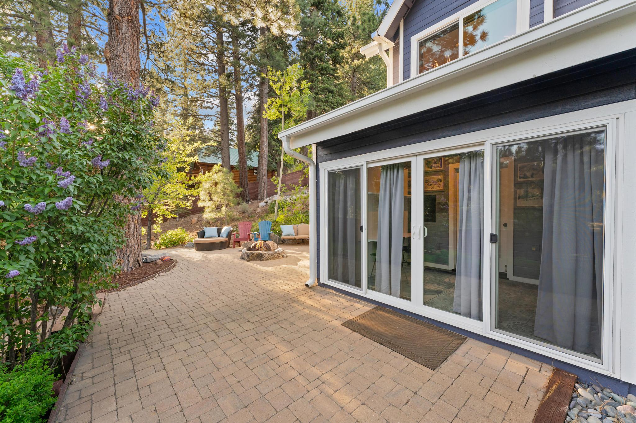 Truckee vacation rental with patio and cozy seating surrounded by tall trees and blooming lilac bush.
