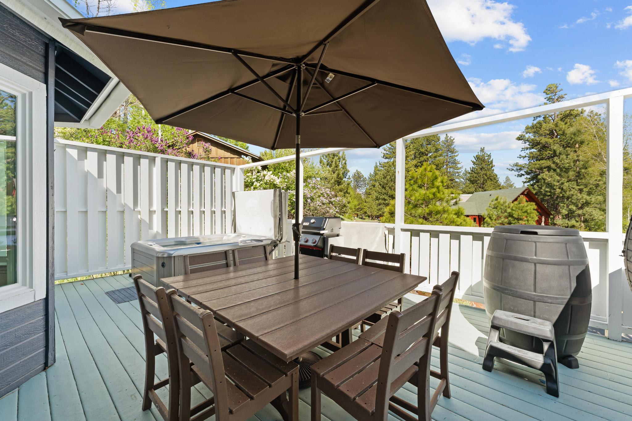 Outdoor deck in Truckee vacation rental with dining set, umbrella, hot tub, and grill, surrounded by greenery.
