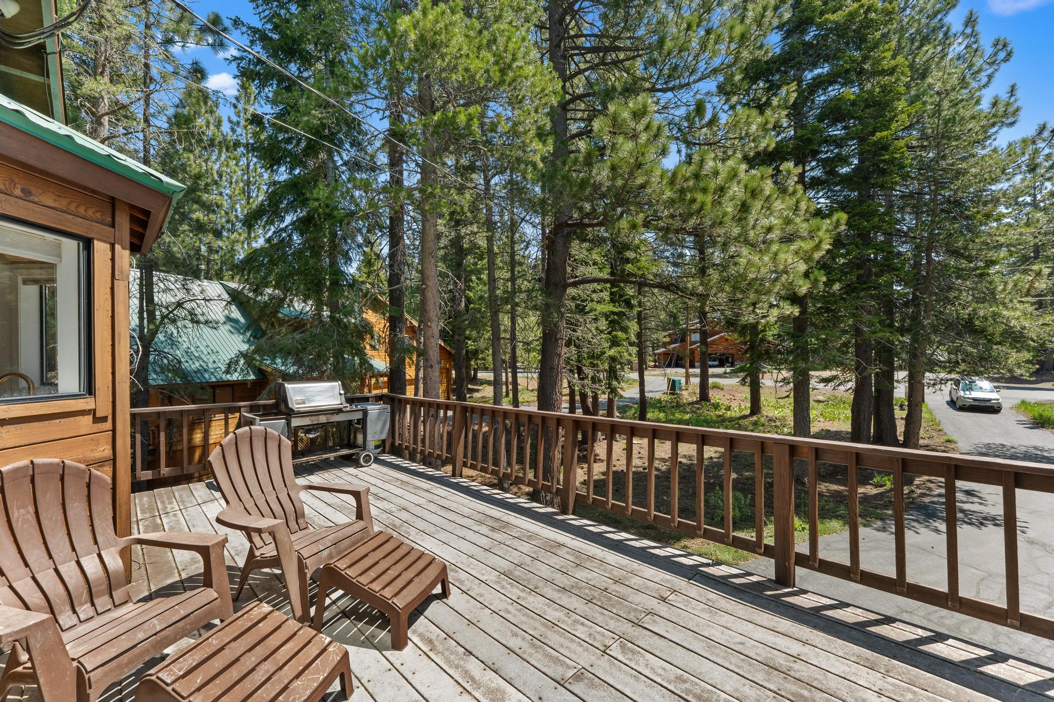 Deck of a Truckee vacation rental with chairs and a grill, surrounded by tall pine trees and a wooded street view.