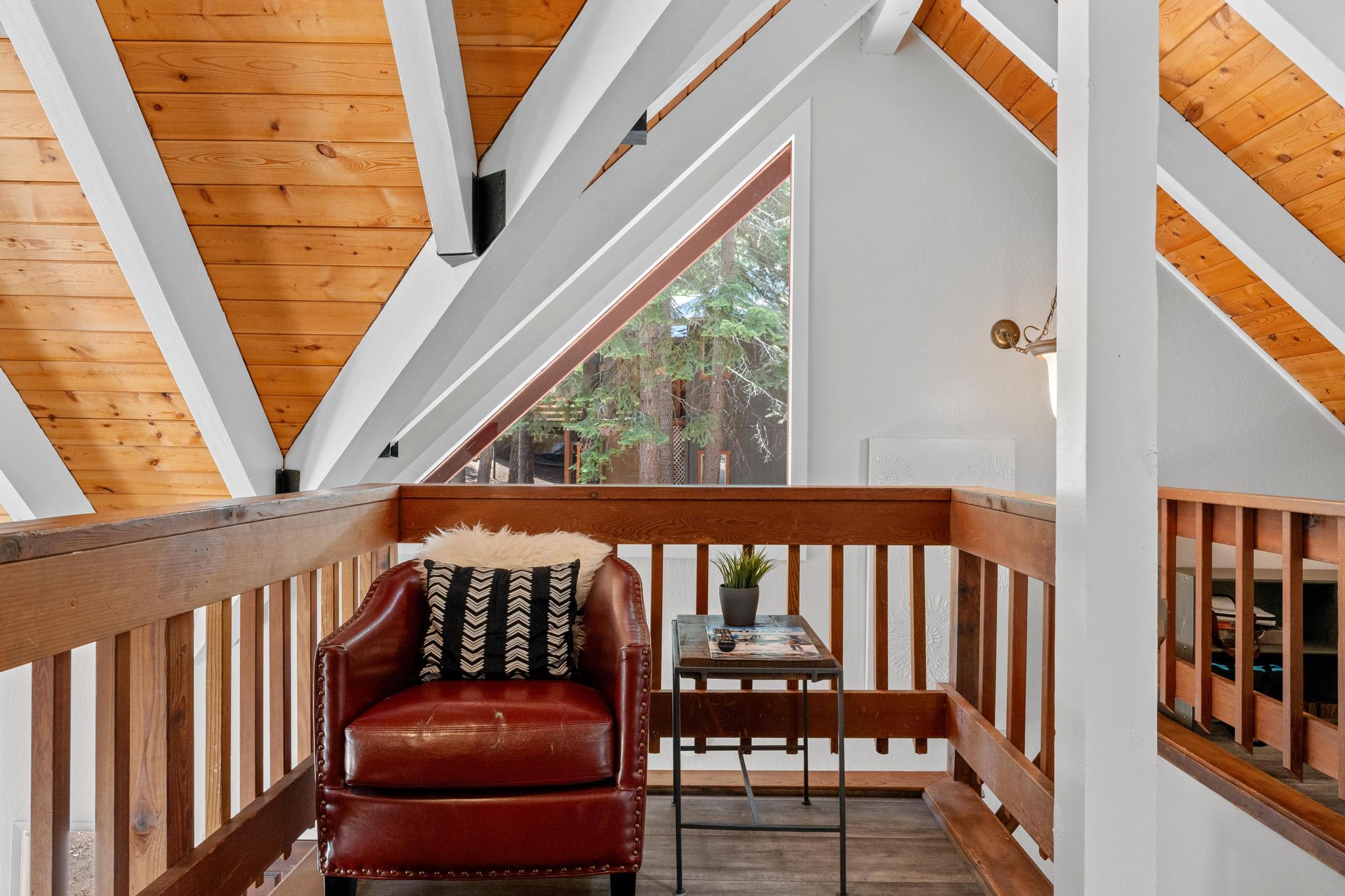 Cozy corner in a Tahoe Vista vacation rental with a red leather chair, wooden beams, and a lush view through a triangle window.