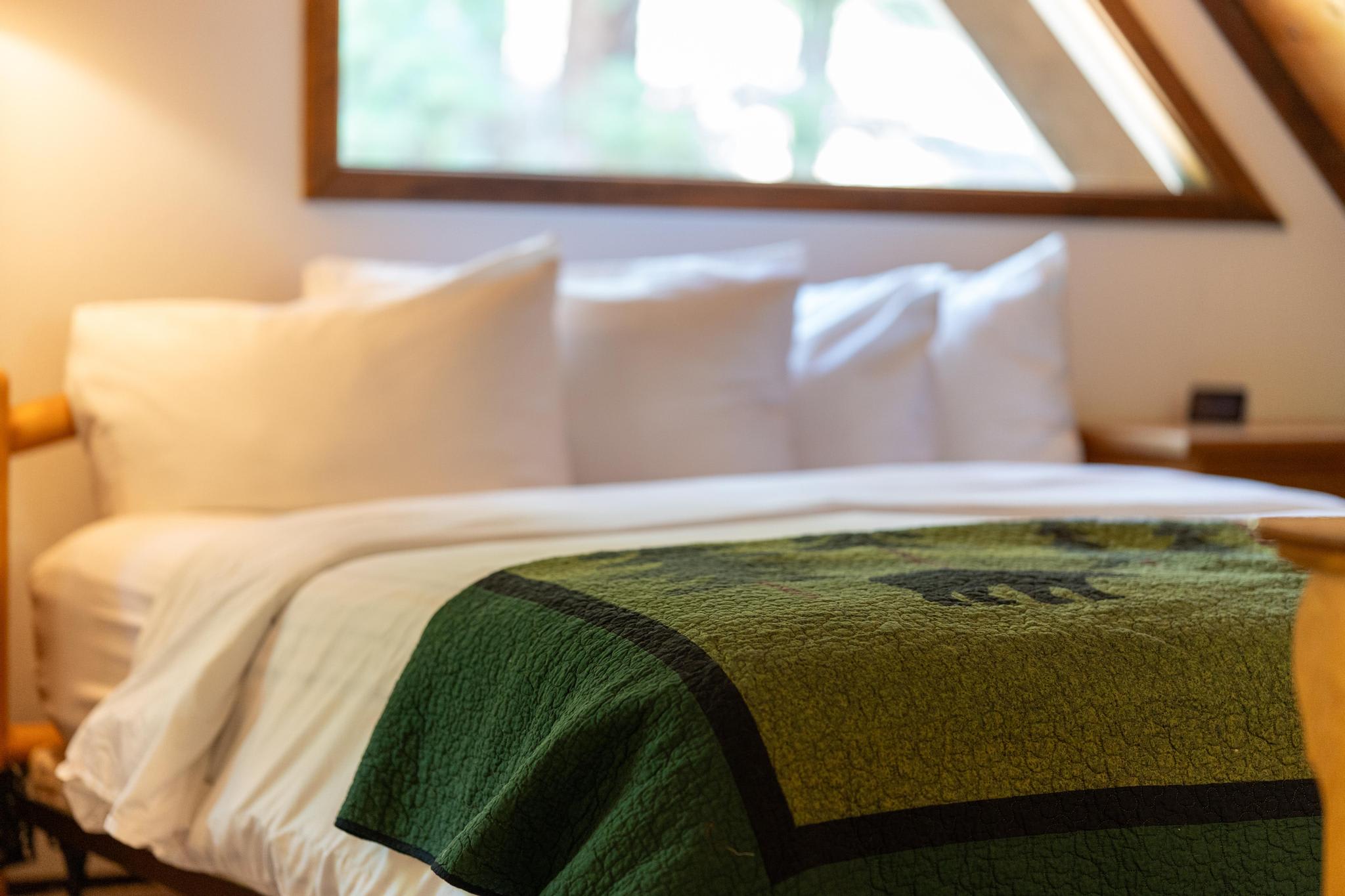 Cozy bedroom in a Tahoe Vista vacation rental with a green quilted bedspread and large triangular window.